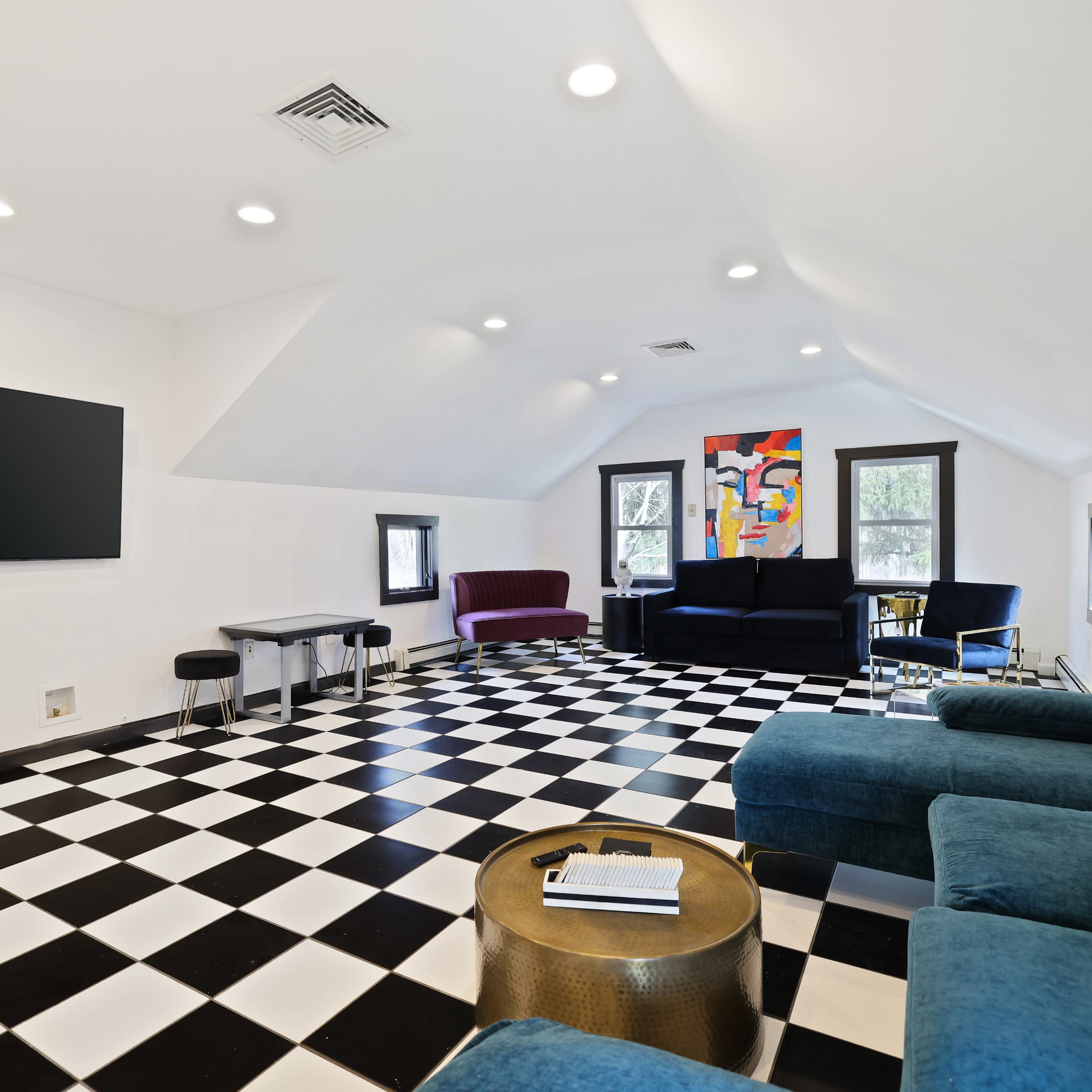 The room features a checkered black and white floor, a large television on the wall, and various seating arrangements, including a blue sectional sofa and two other chairs.