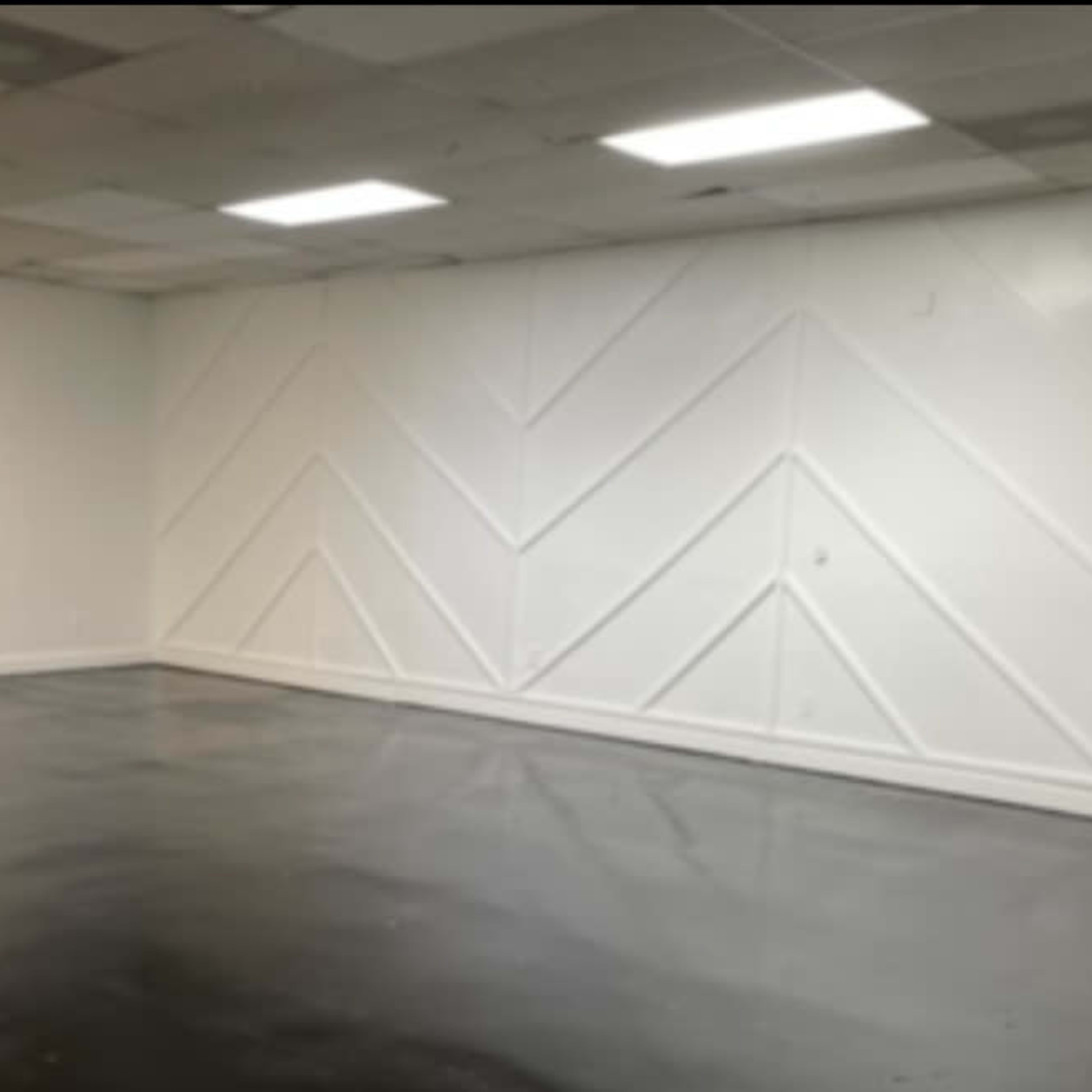 A spacious room with a polished floor and a white wall featuring a geometric pattern.