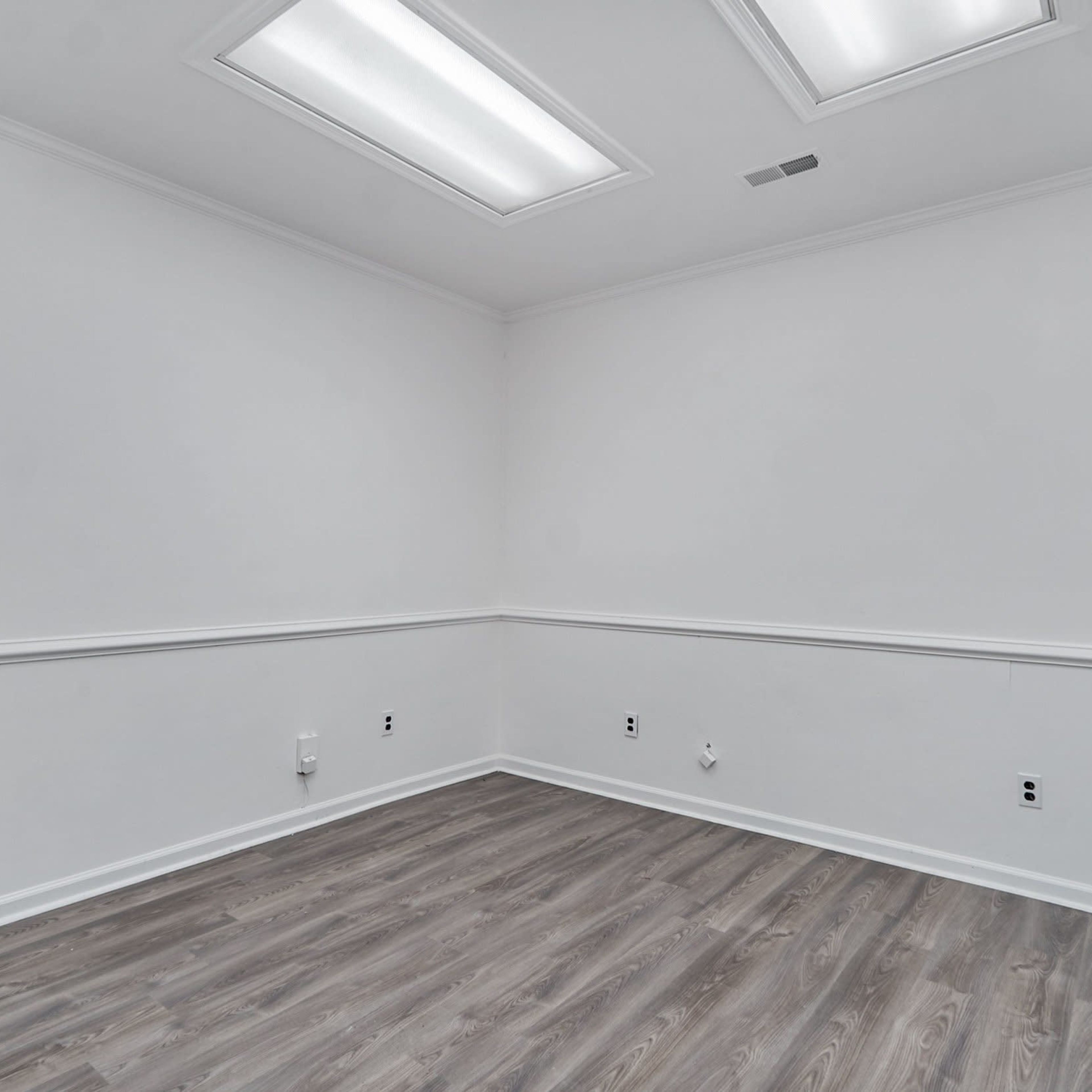 An empty room with white walls, a wooden floor, and two ceiling lights.