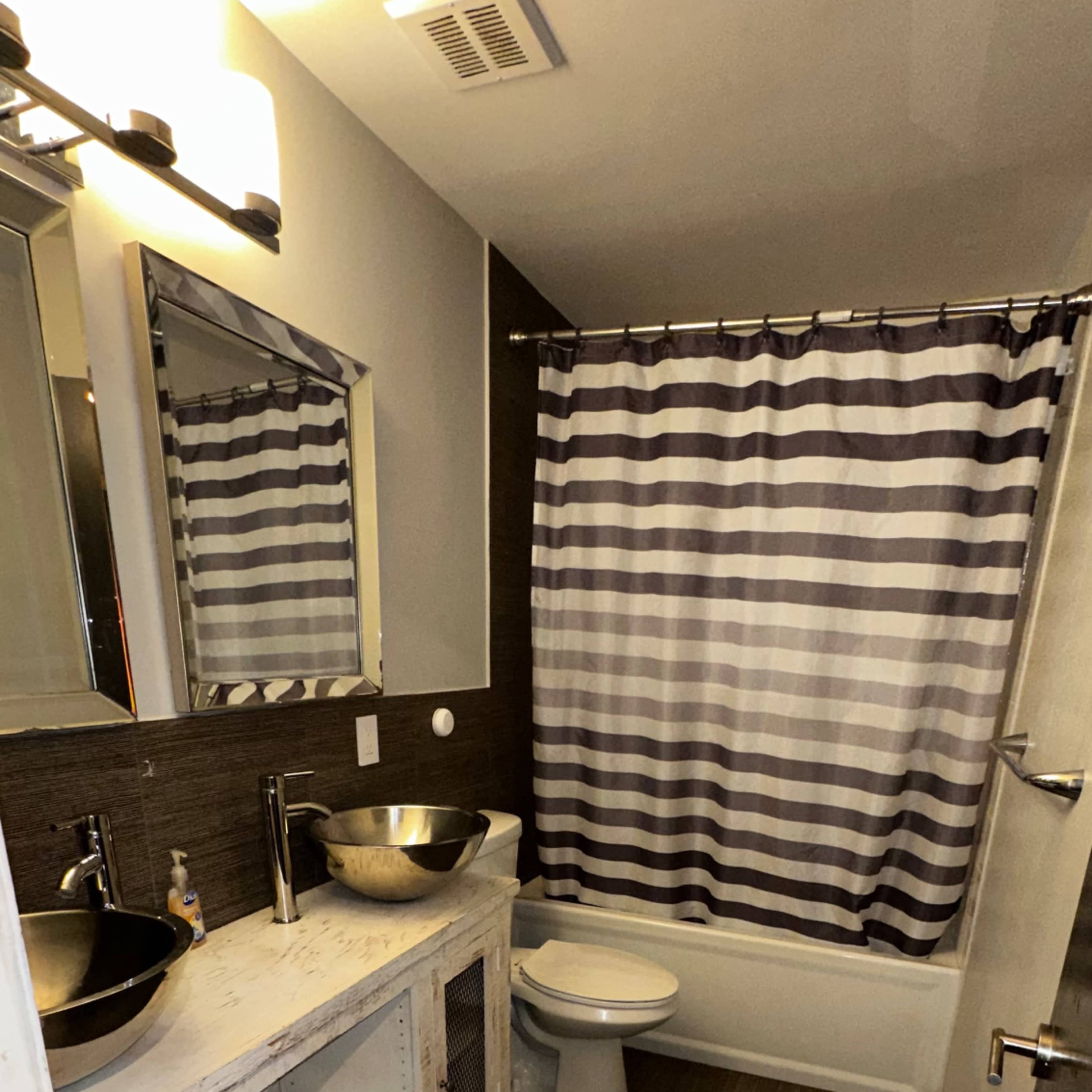 A modern bathroom features a white bathtub, striped shower curtain, two mirrors above a wooden sink vanity, and tiled flooring.