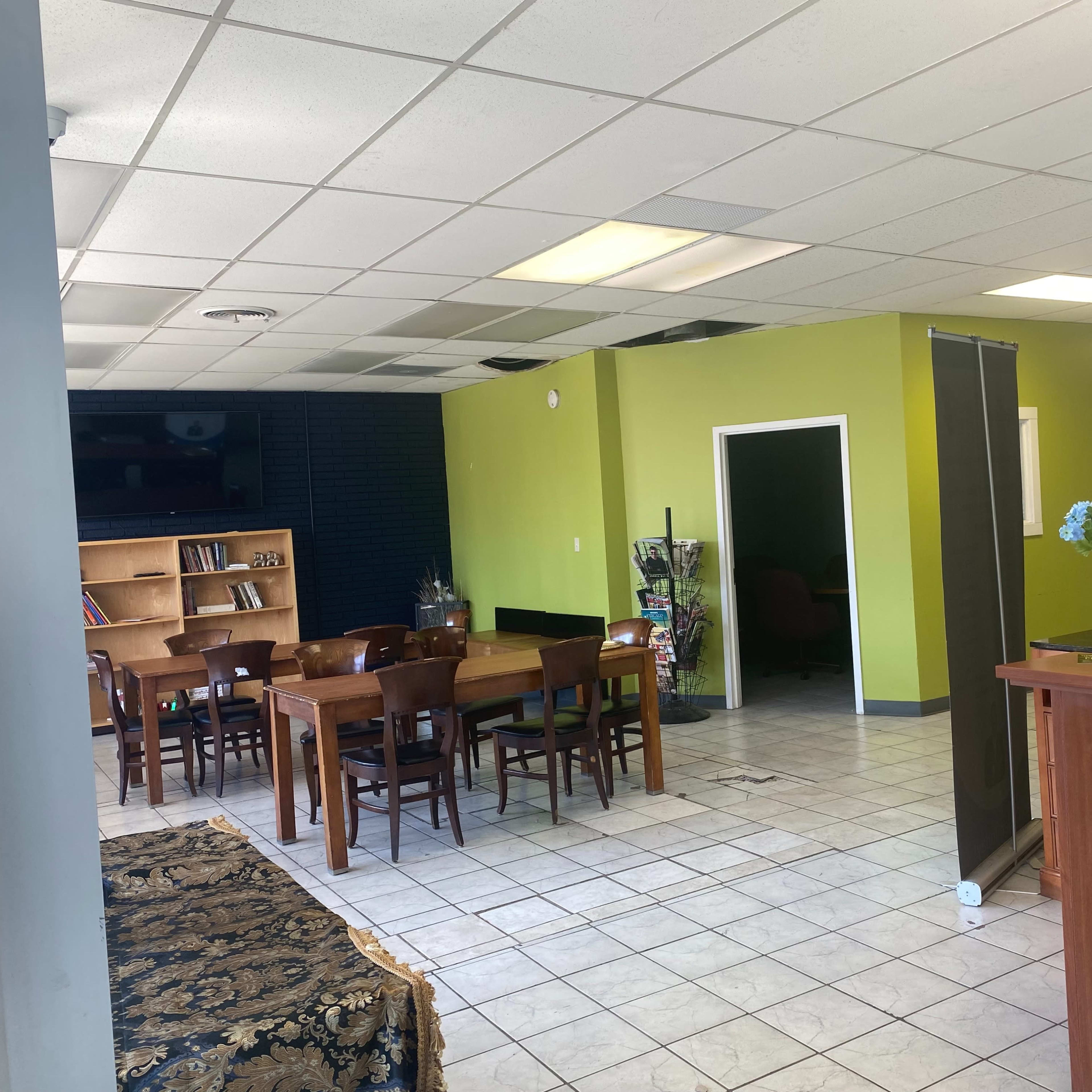 A spacious interior with tables and chairs on one side, a reception desk on the other, and a green accent wall separating the two areas.