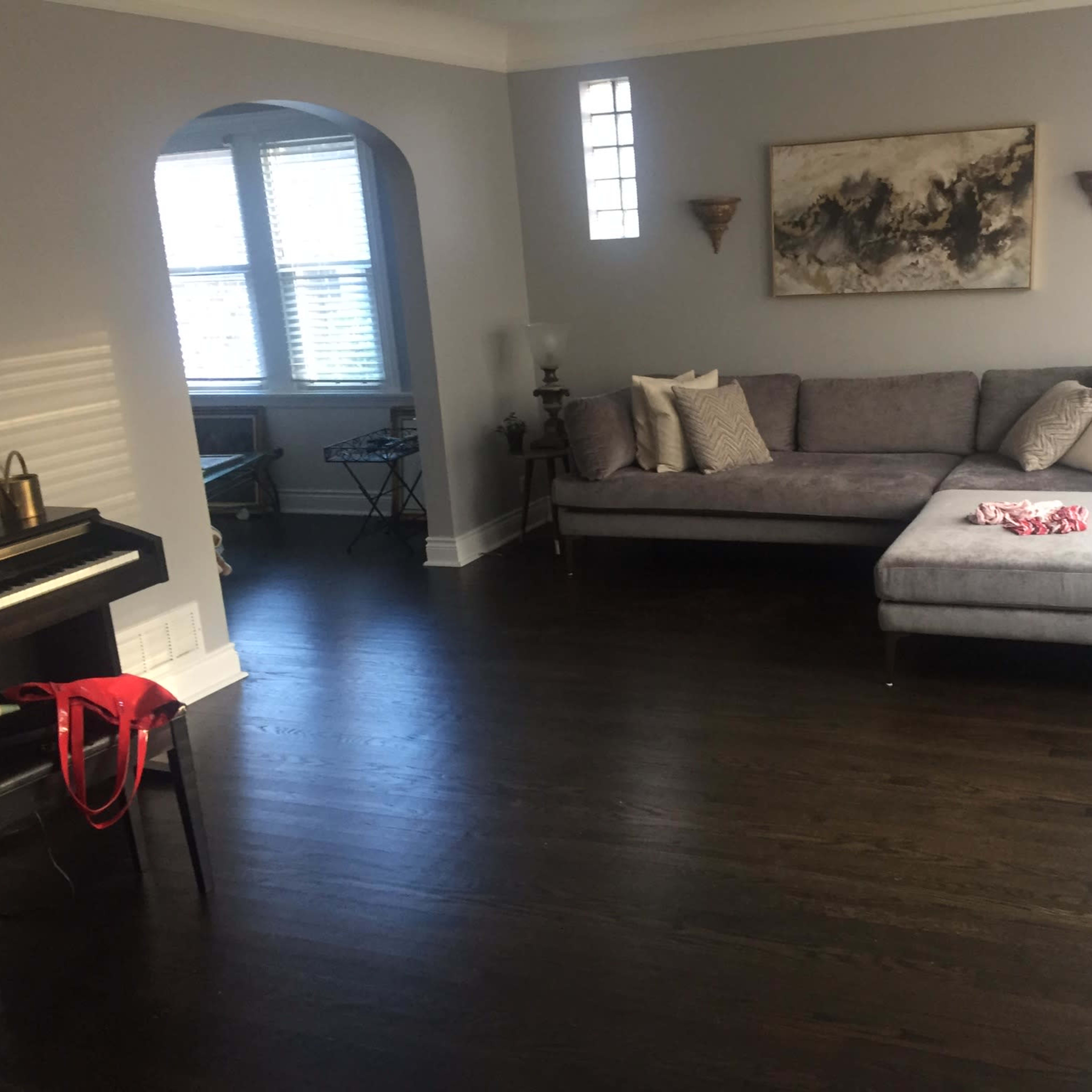 A living room featuring a gray sectional couch, a piano, and a window archway.