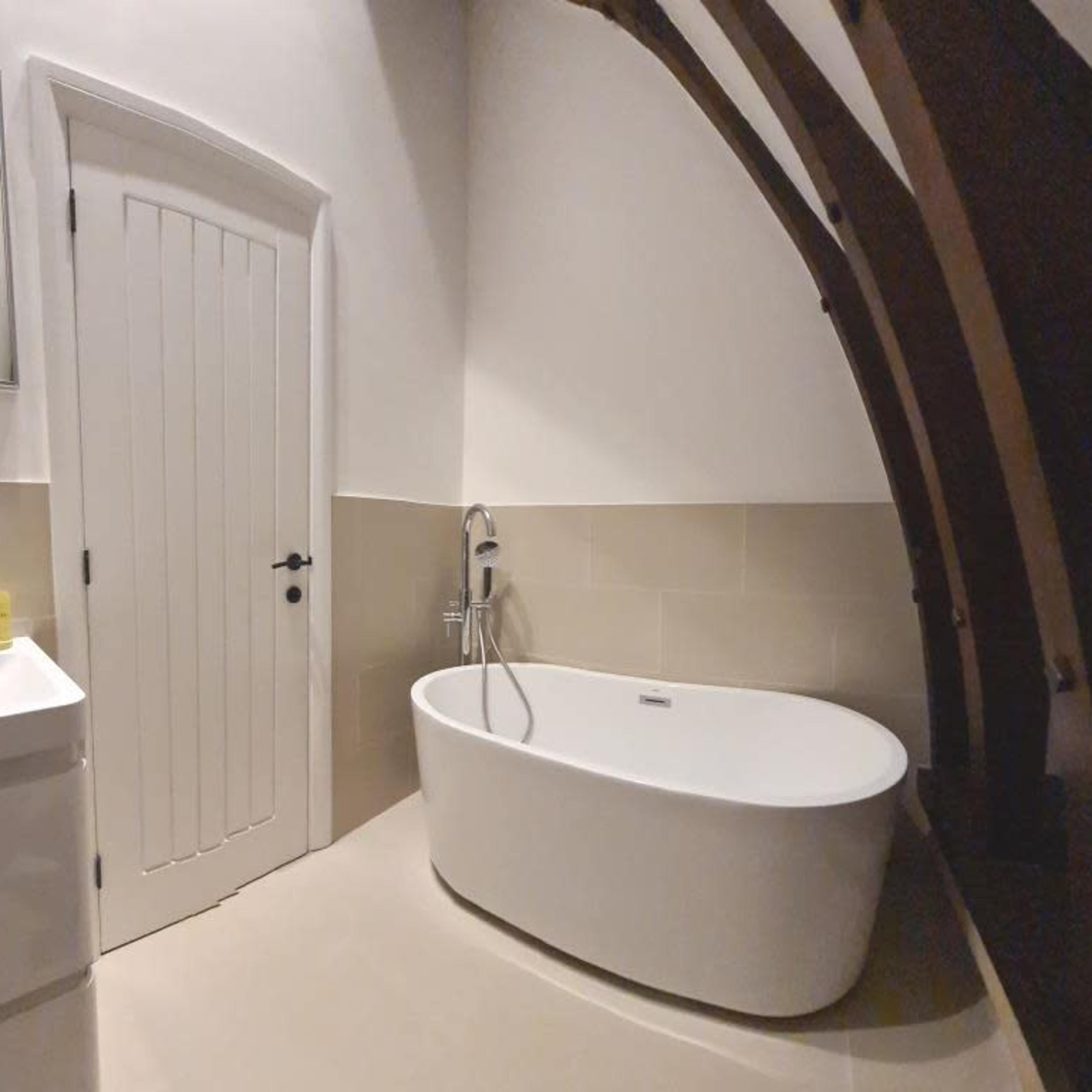 A modern bathroom featuring a freestanding bathtub, a wall-mounted sink, and a large mirror, with wooden beams accentuating the curved ceiling.
