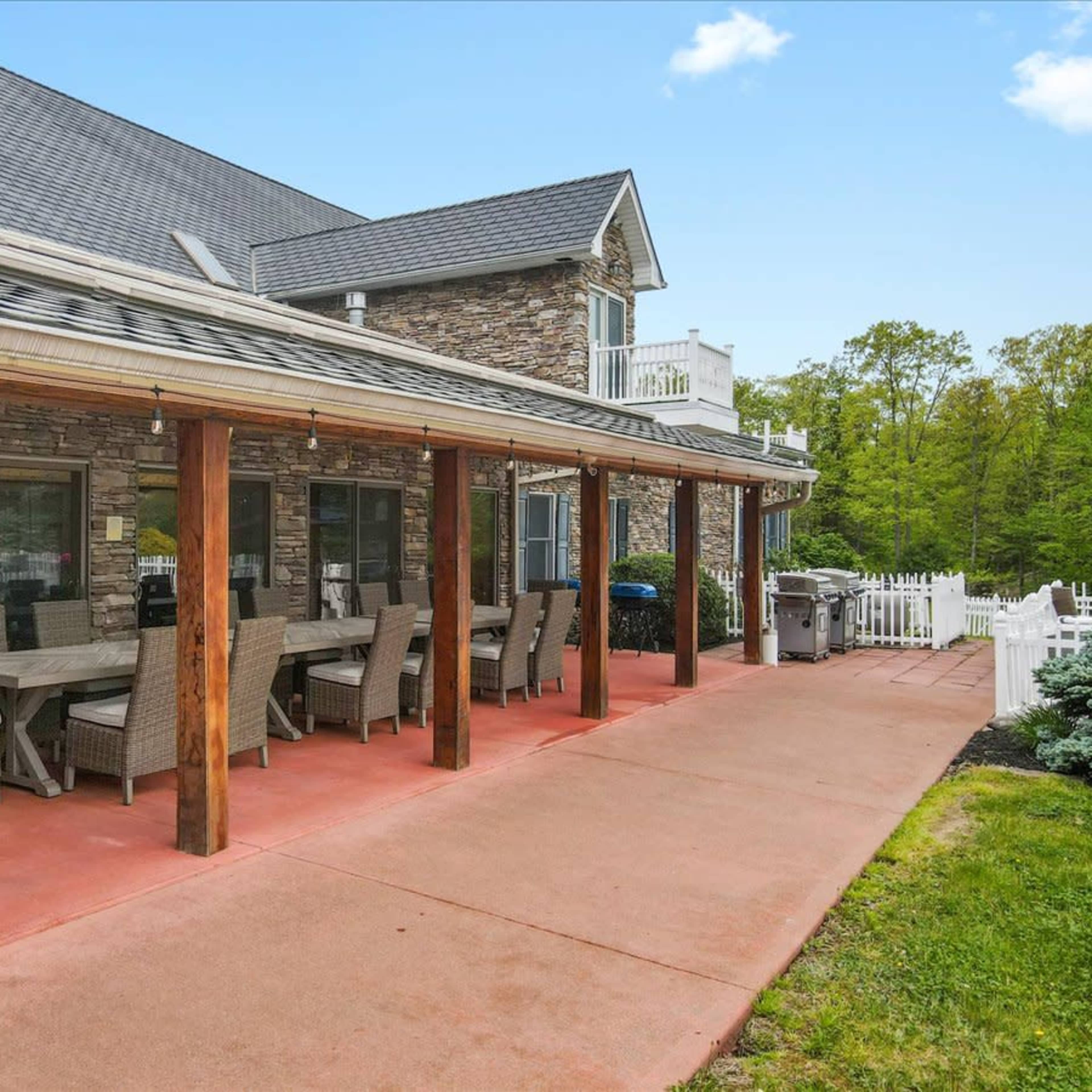 A spacious patio with a long dining table and chairs, adjacent to a large stone building.