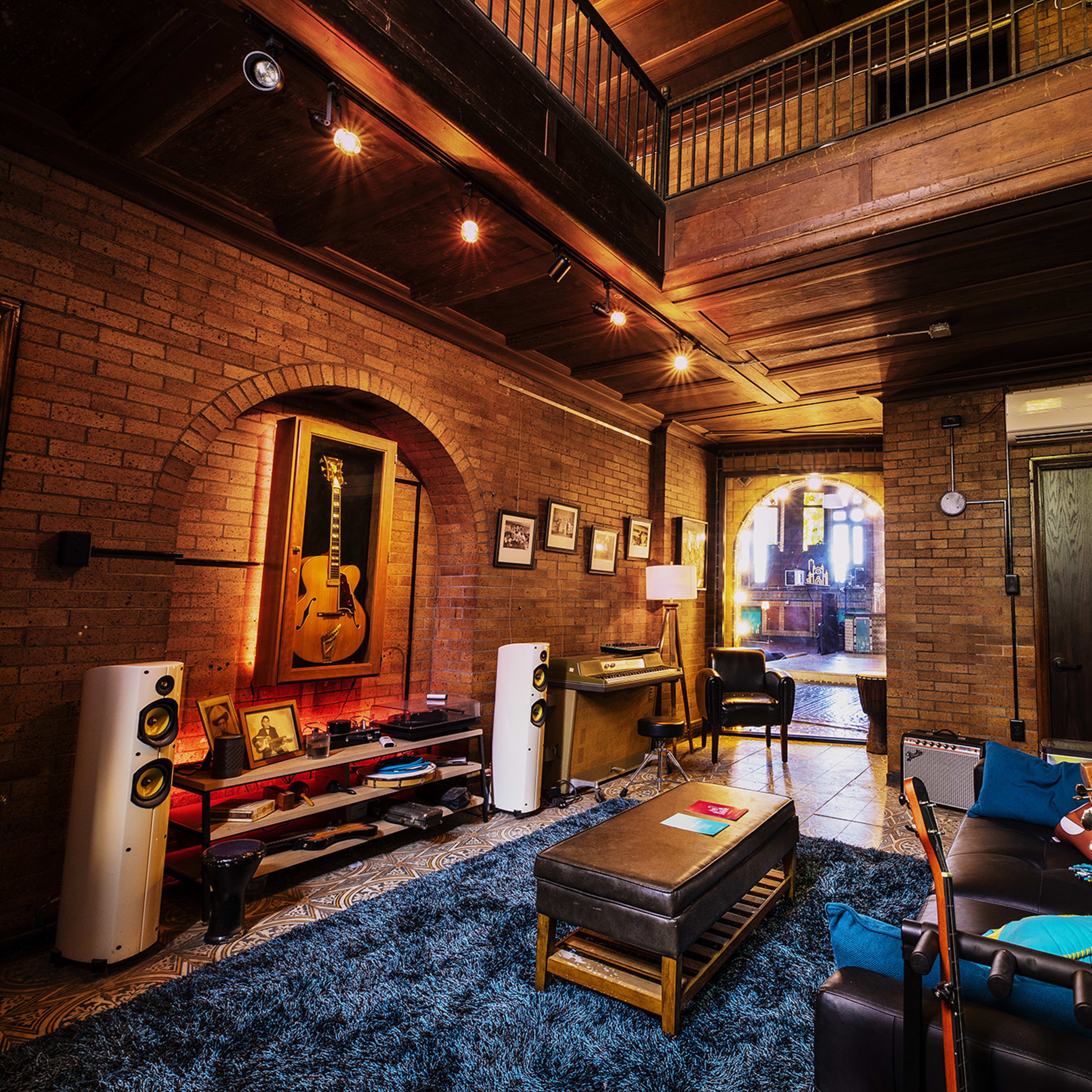 A spacious living room with exposed brick walls, wooden beams, and a blue accent wall, furnished with a couch, a coffee table, and audio equipment.