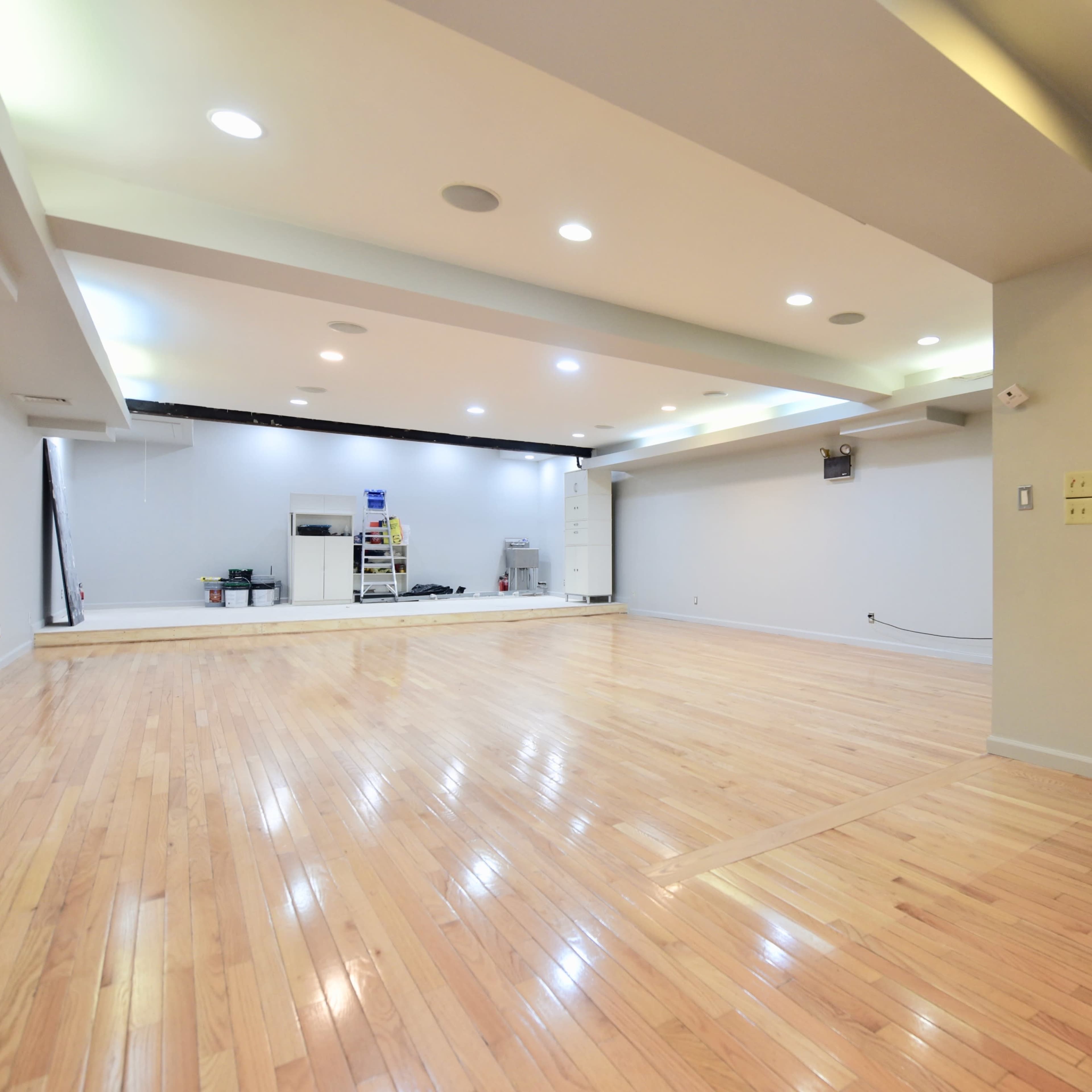 A spacious, well-lit room with polished wooden flooring and an adjacent bathroom entrance.