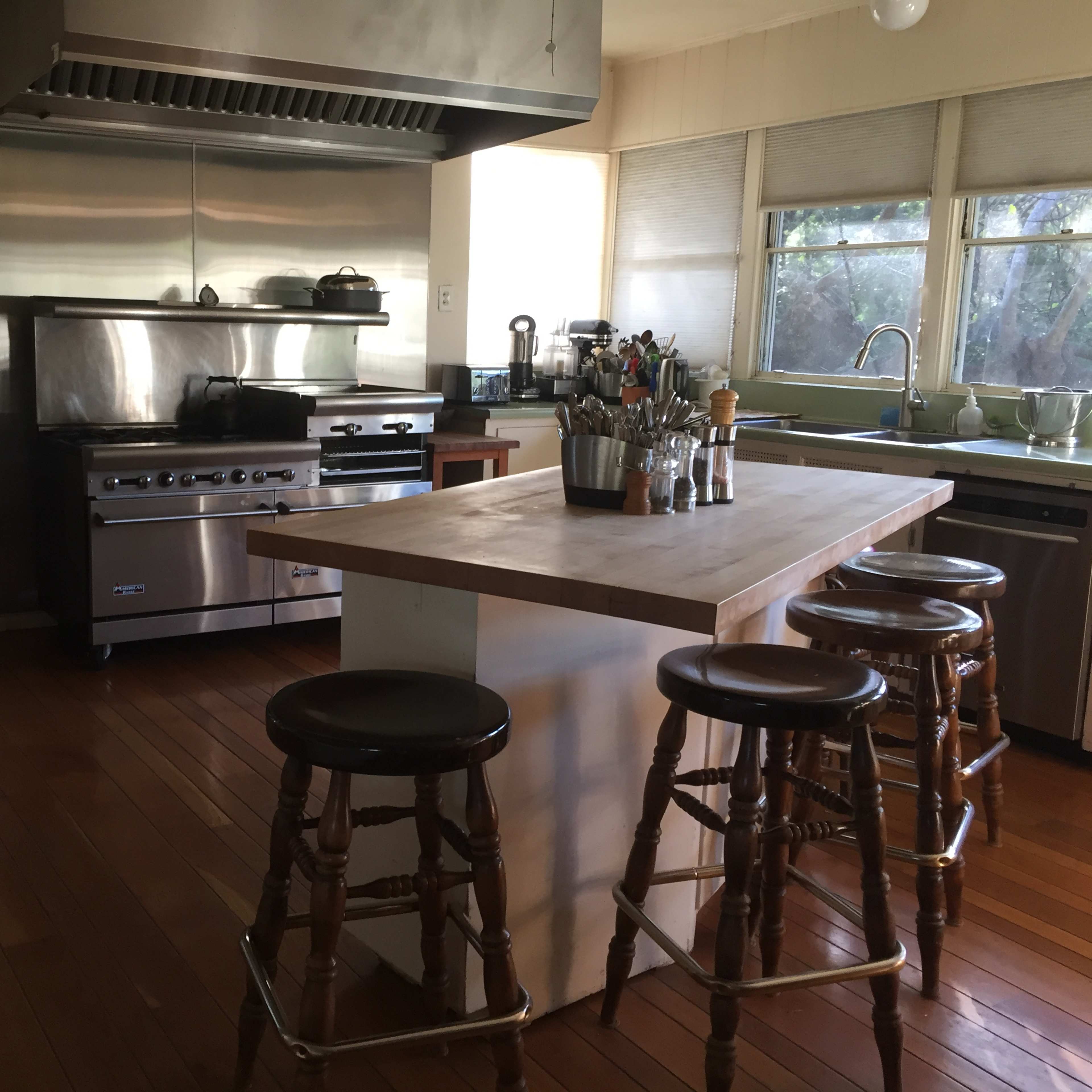 The kitchen features stainless steel appliances, a large island with bar stools, and a window allowing natural light.