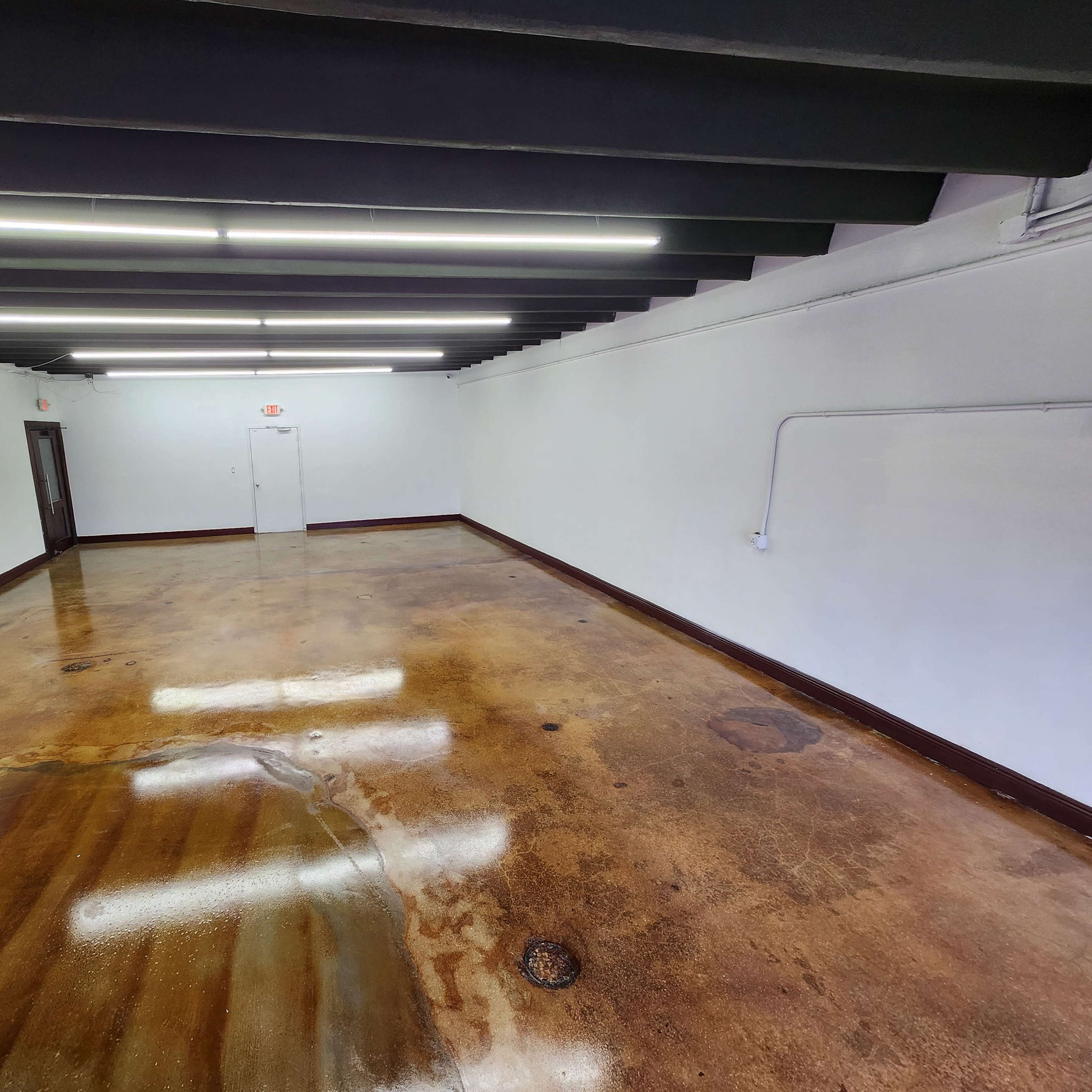 An empty room with a polished concrete floor, white walls, and fluorescent lighting along the ceiling.