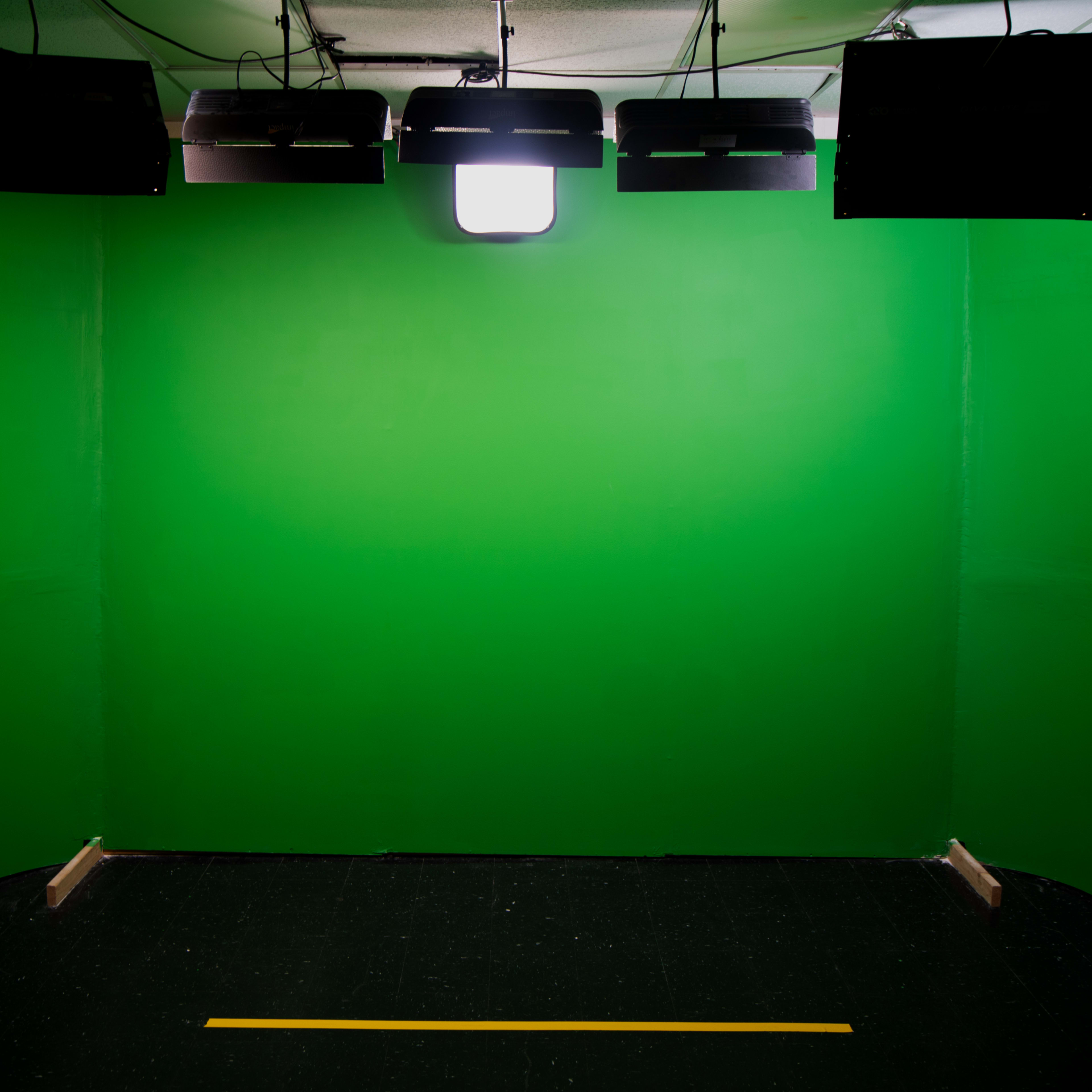 A plain green studio with spotlights mounted on the ceiling, designed for video production.