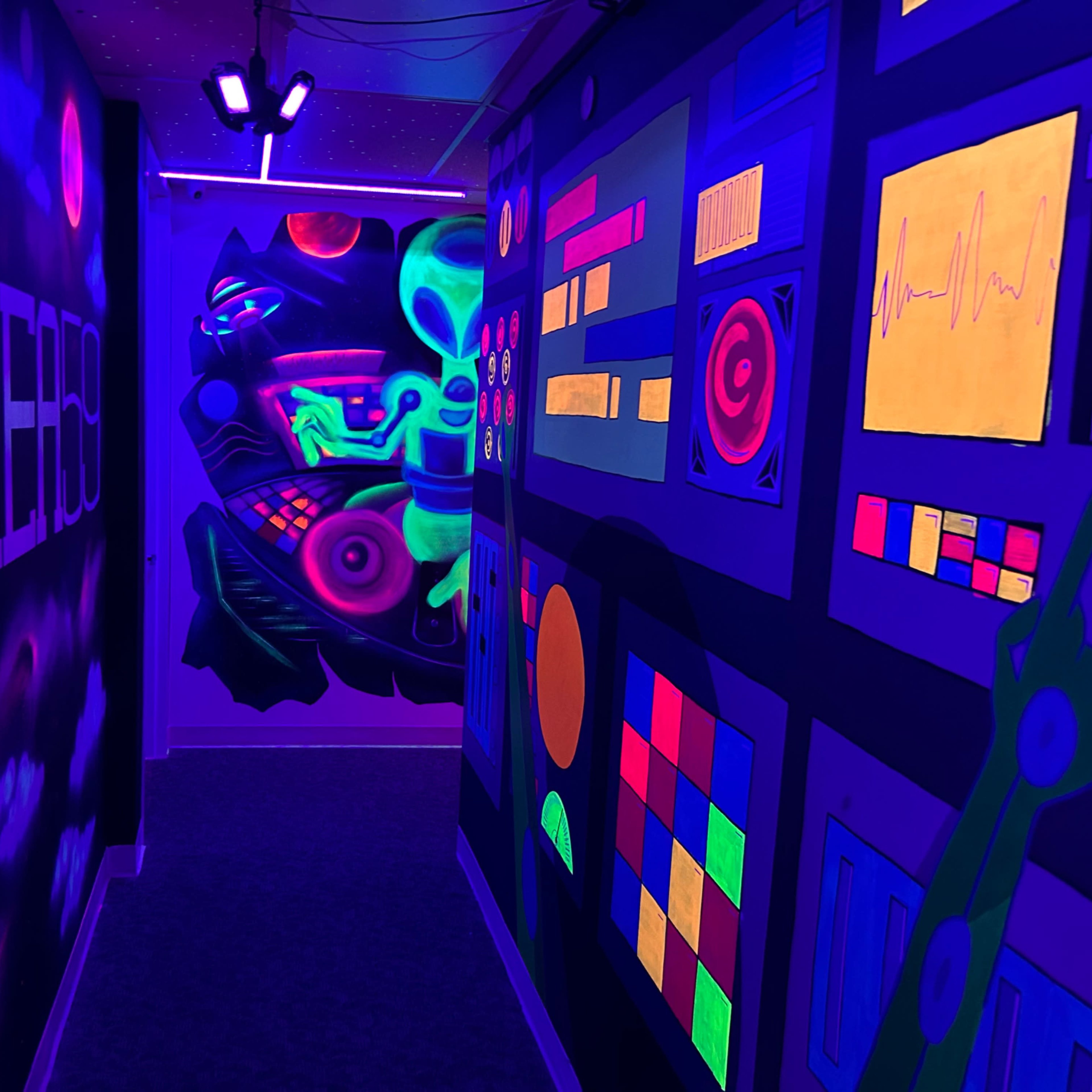 A colorful hallway illuminated by black lights, featuring vibrant murals on the walls depicting abstract shapes and futuristic designs.