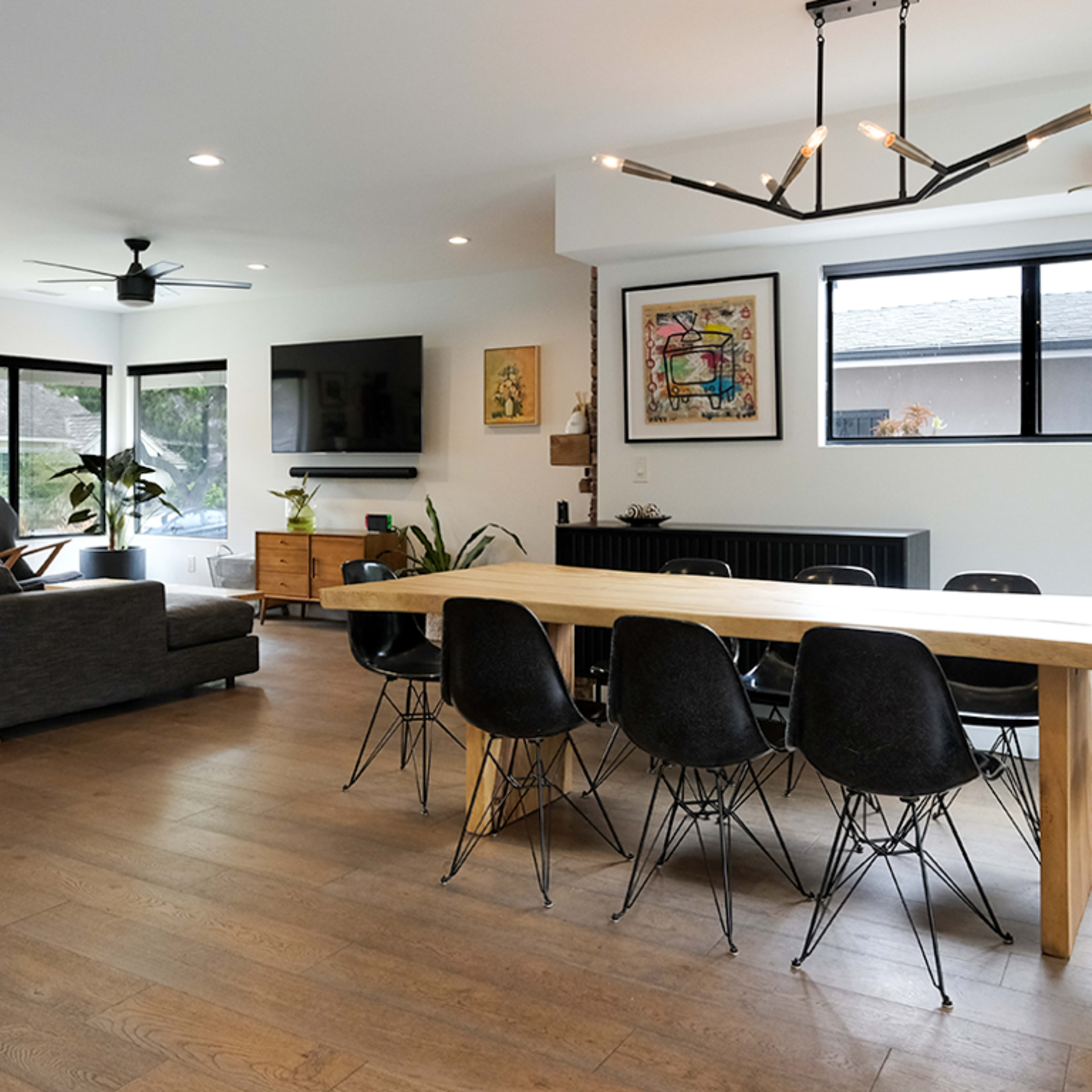 A modern living and dining area with a large wooden table, black chairs, a gray sofa, and a dog resting on the floor.