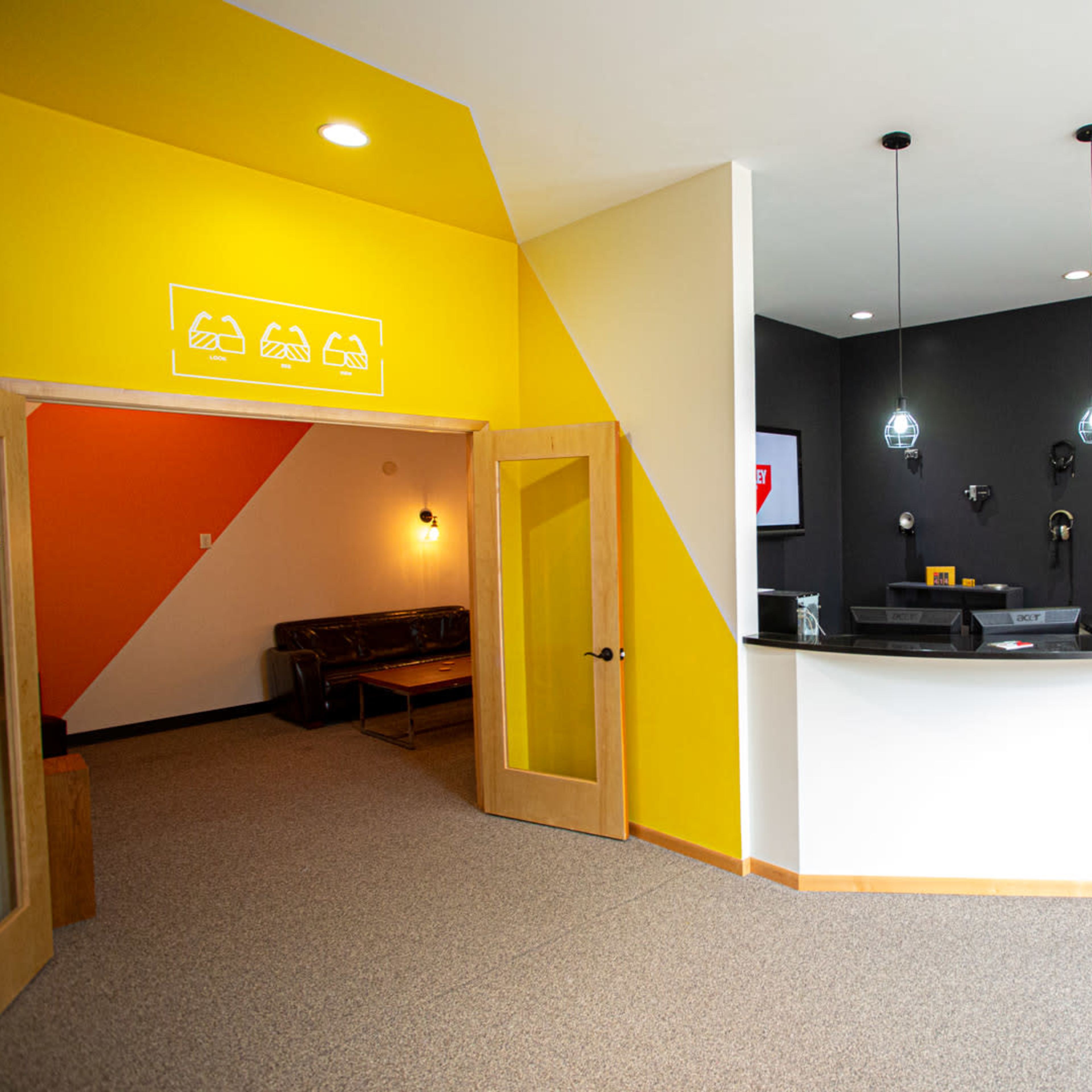 A modern reception area with a yellow and black geometric design, featuring a reception desk, seating area, and access to additional rooms.