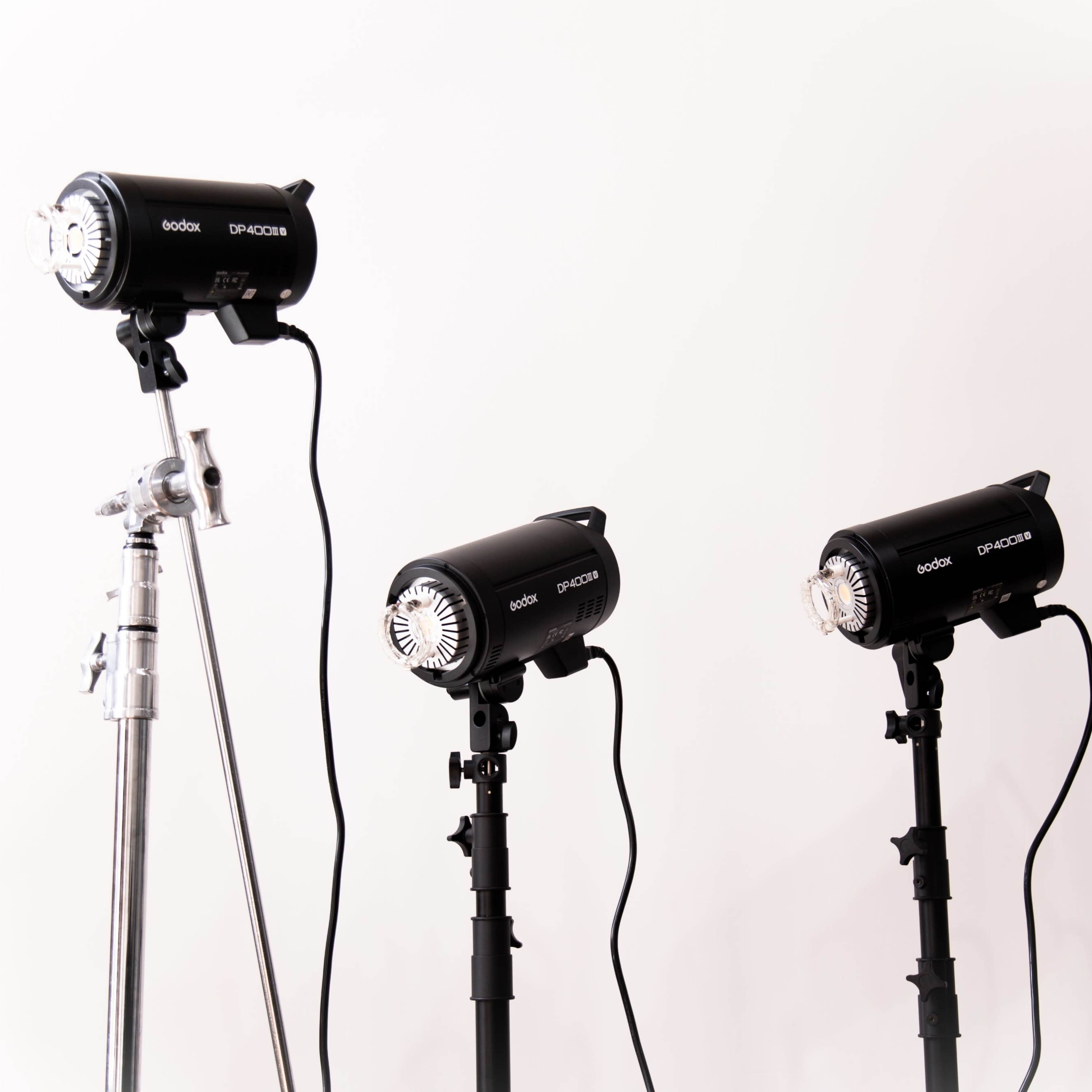 Three studio lights are positioned on stands against a white background.