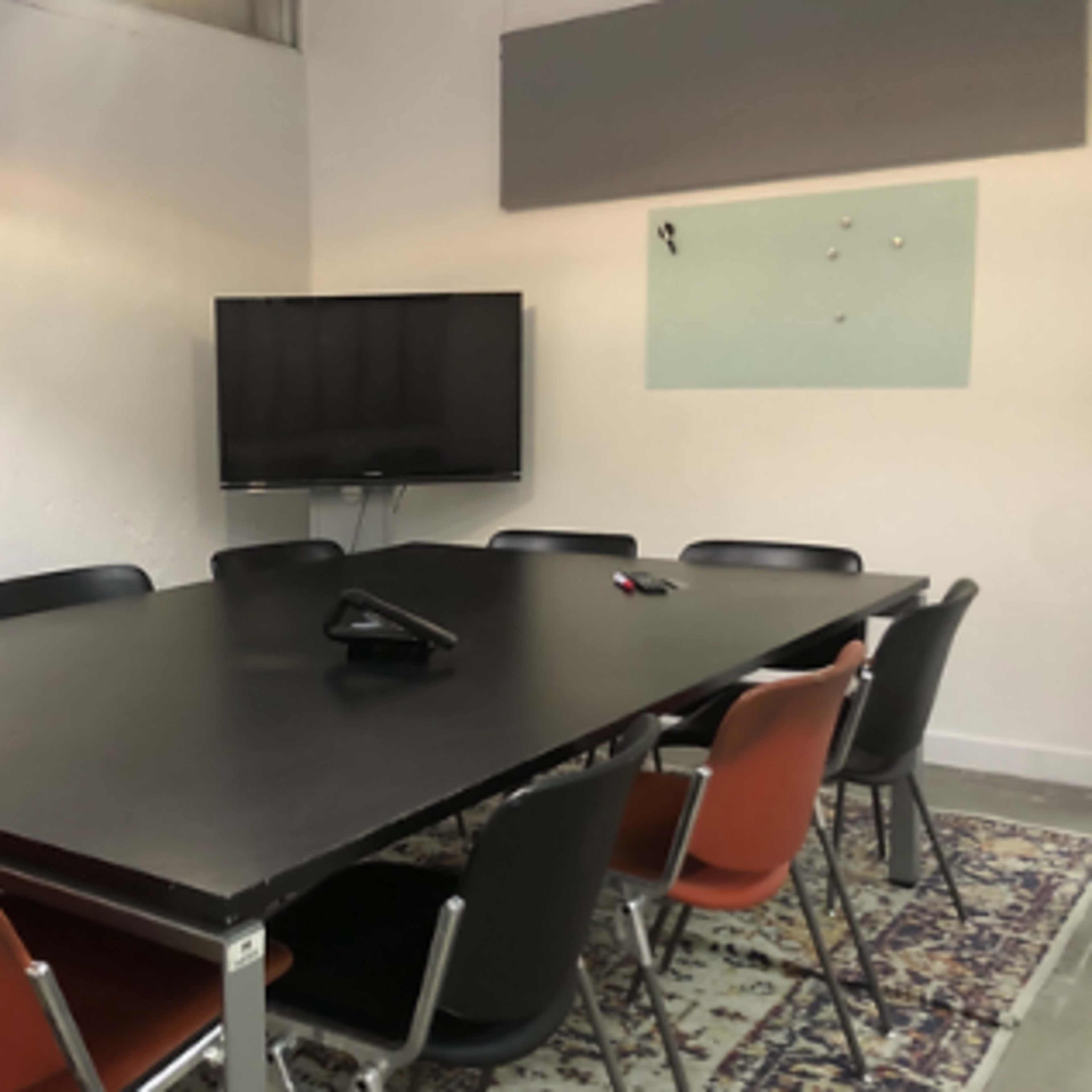 A conference room with a large black table surrounded by several chairs and a television mounted on the wall.
