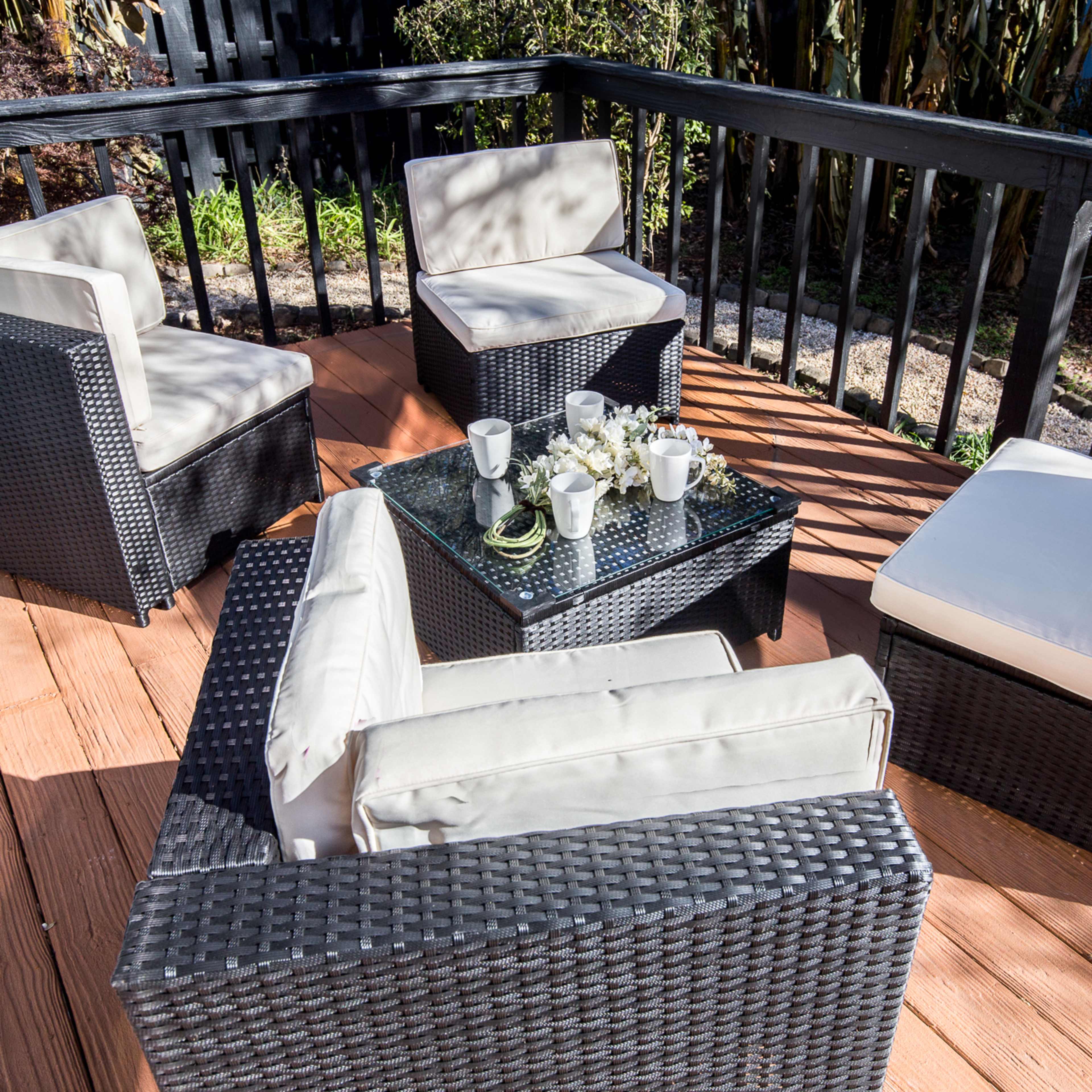 A seating area with four cushioned chairs surrounding a glass-topped table is positioned on a wooden deck.
