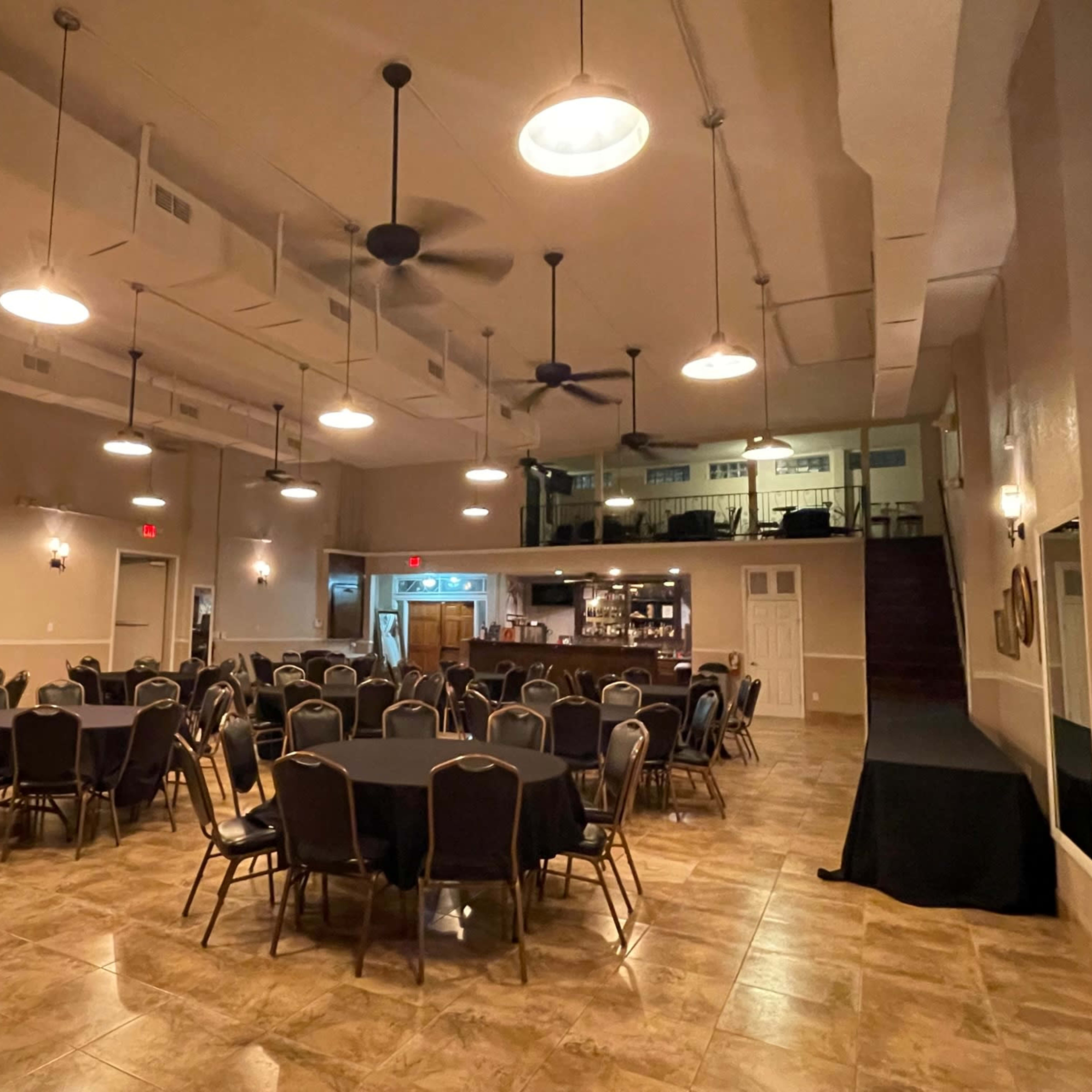 A large event space with round tables set for dining and a stage area in the background.