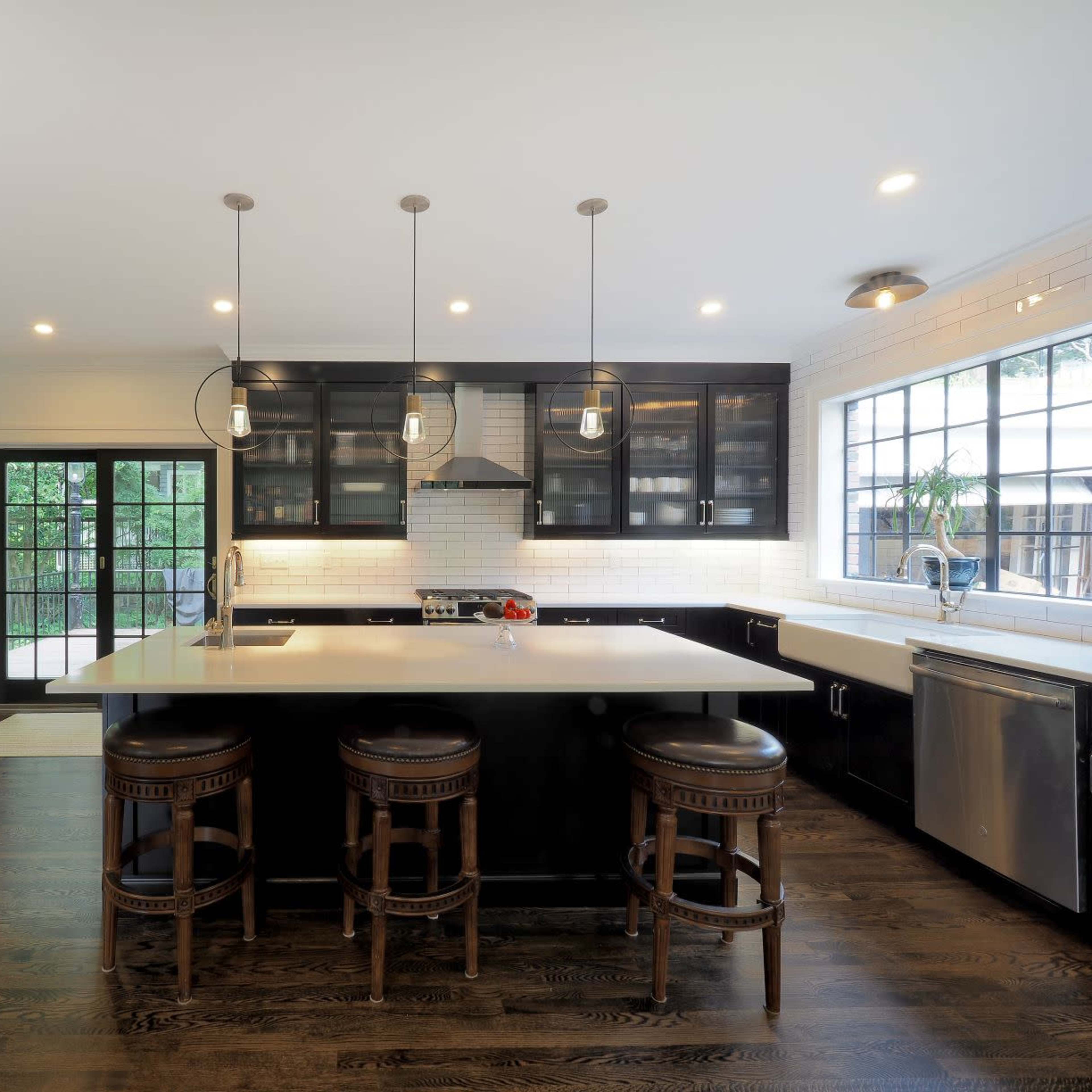 A modern kitchen with dark cabinets, a large island with three stools, and stainless steel appliances.