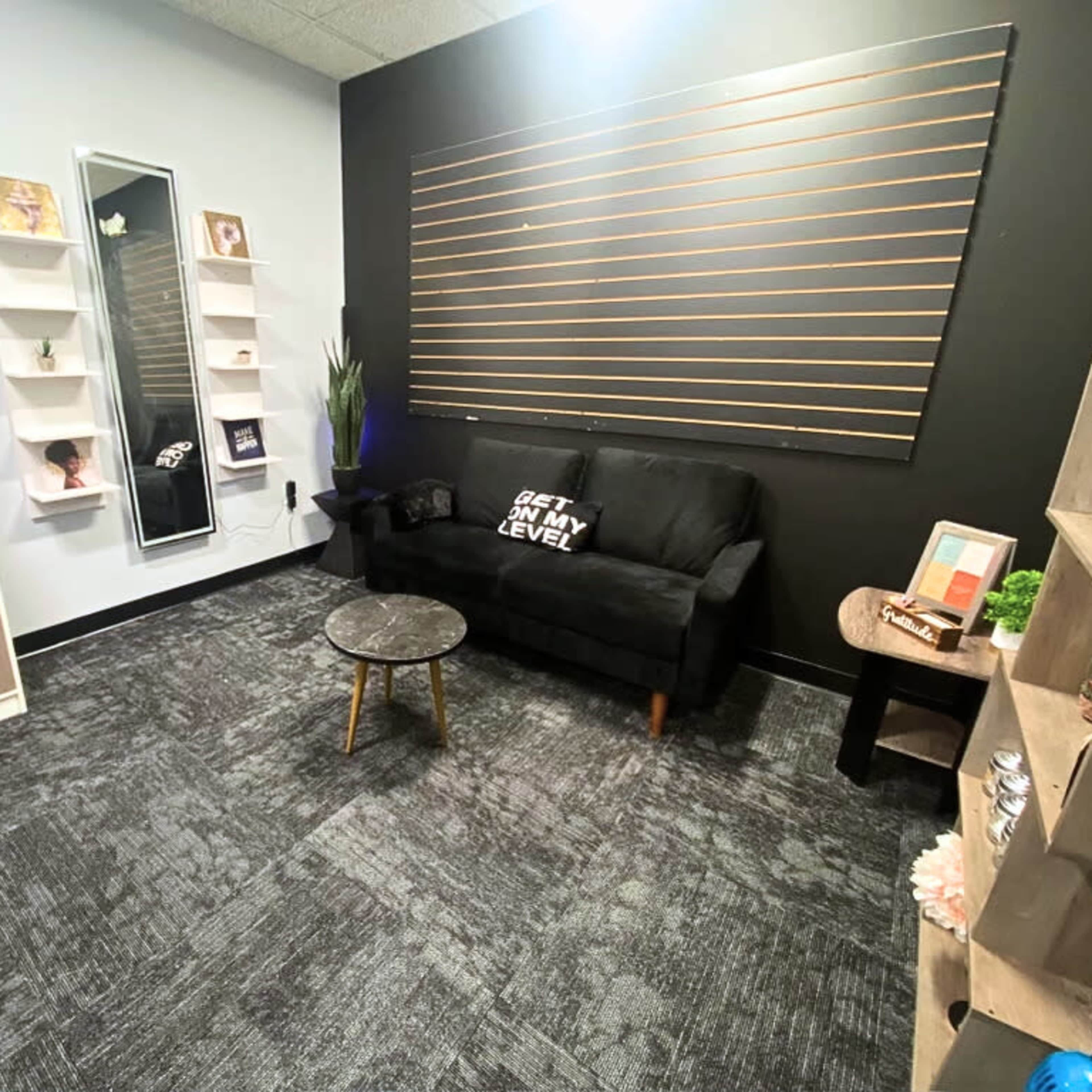 A small, modern interior room featuring a black sofa, a round table, and decorative shelves against a dark wall.