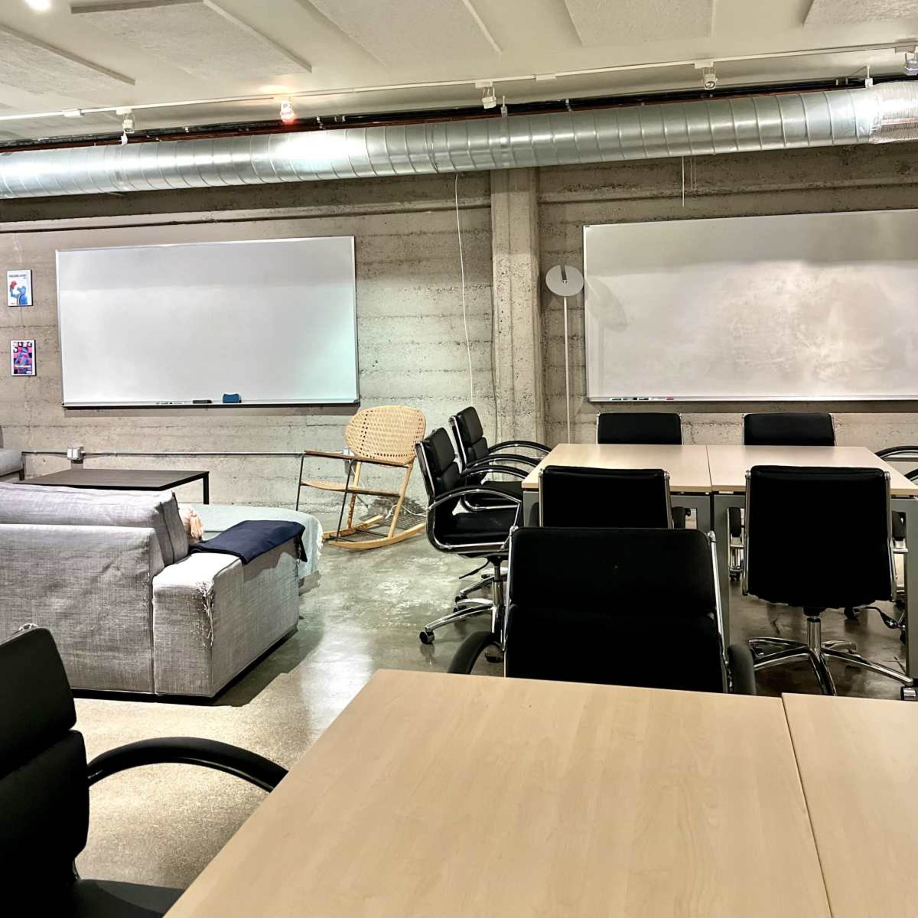 A modern office space with a mix of seating, including a sofa, rocking chair, and several black office chairs around wooden tables.