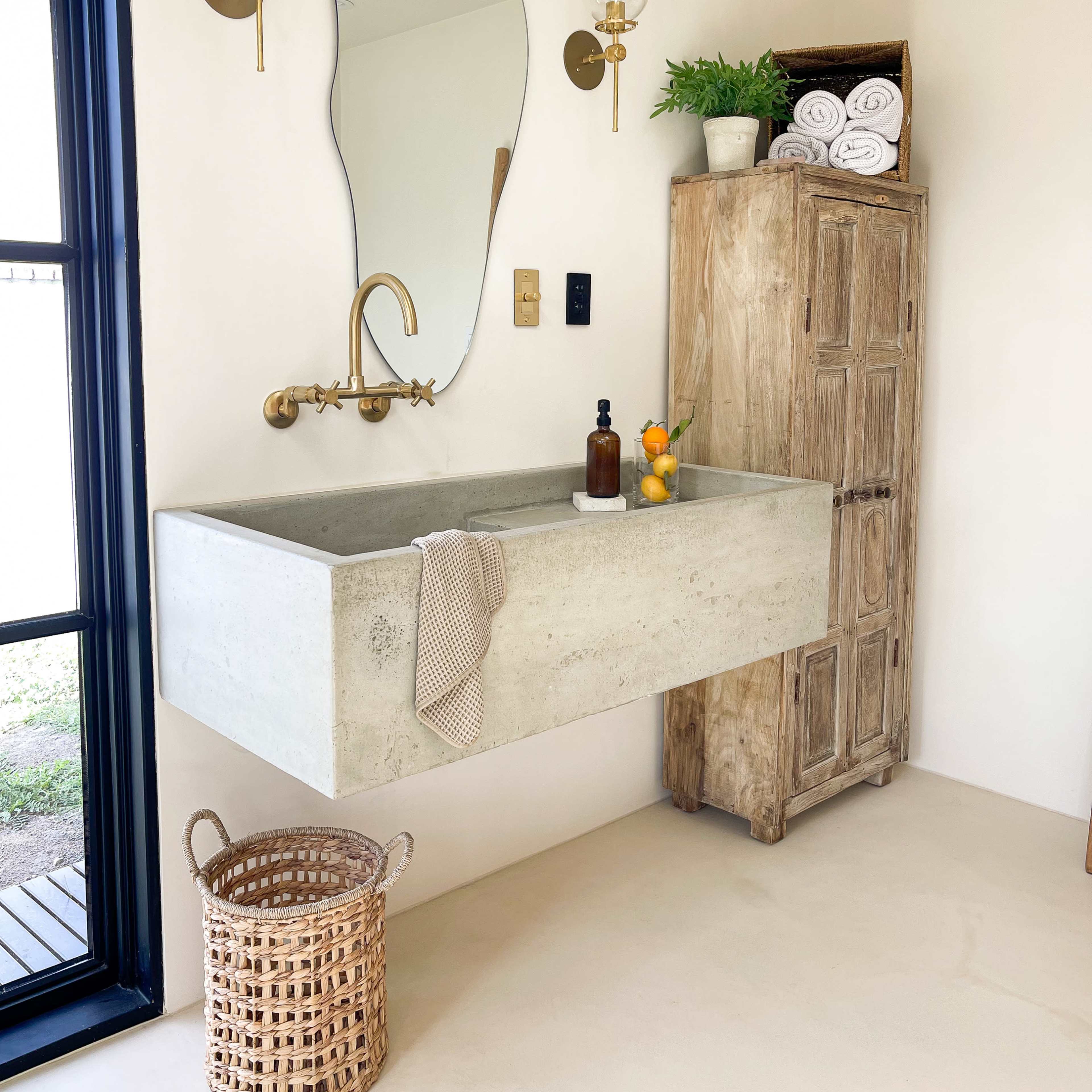 A minimalist bathroom with a concrete sink, a large mirror above it, a wooden cabinet on the right, and a wicker basket on the floor.