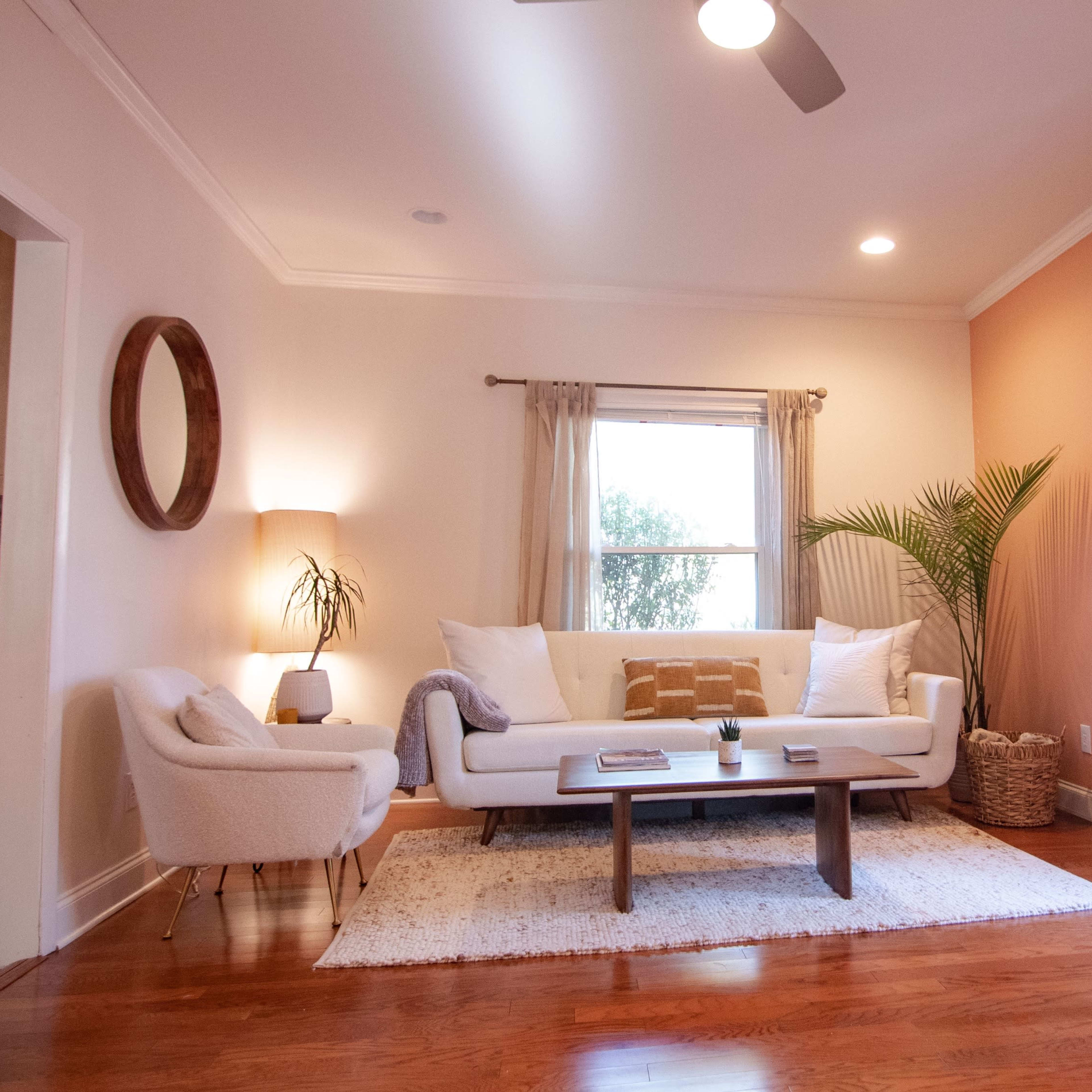 A modern living room features a white sofa, a coffee table, and large windows with natural light.
