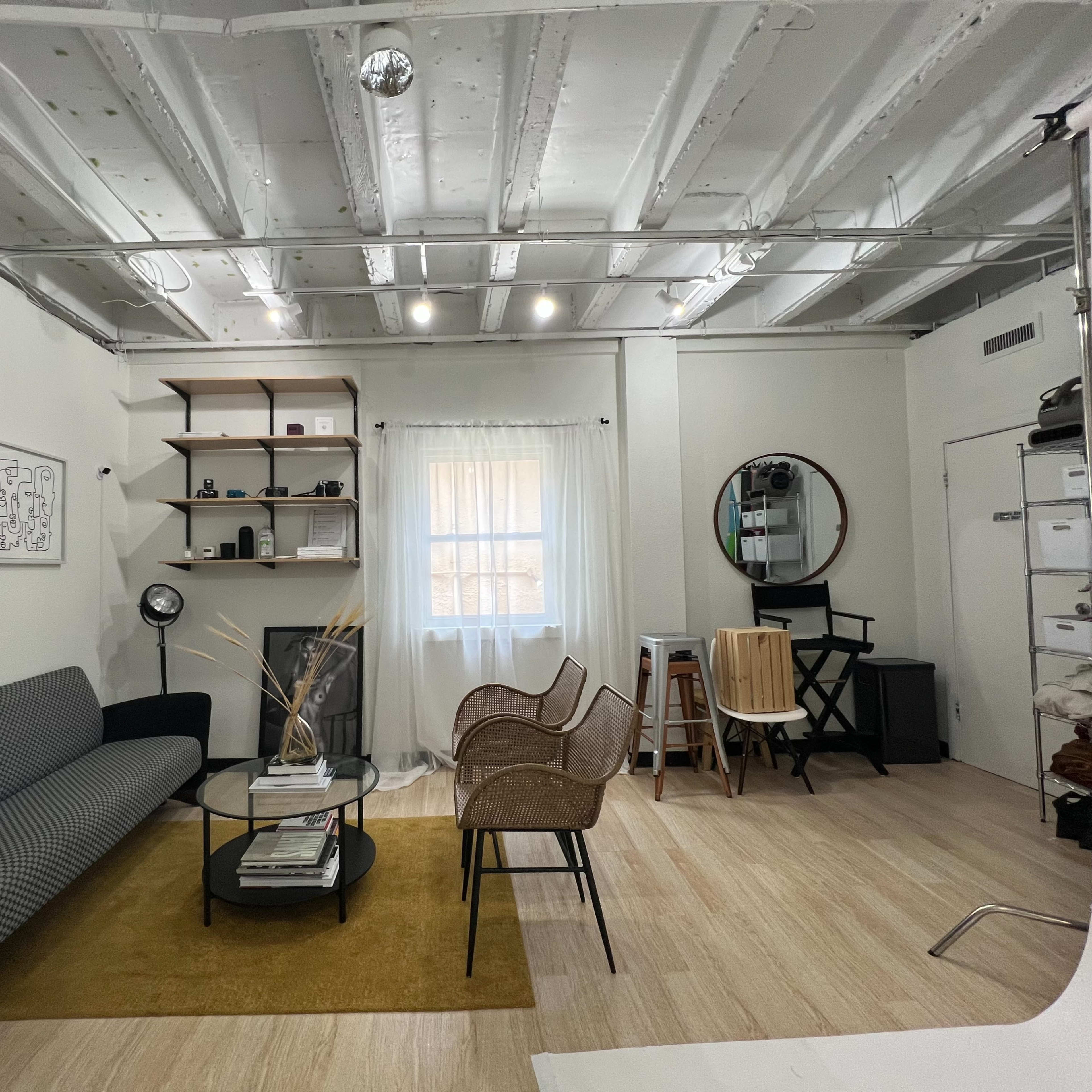 A modern living area with a gray couch, a round glass coffee table, a rug, and various furniture items including chairs and shelves against the walls.