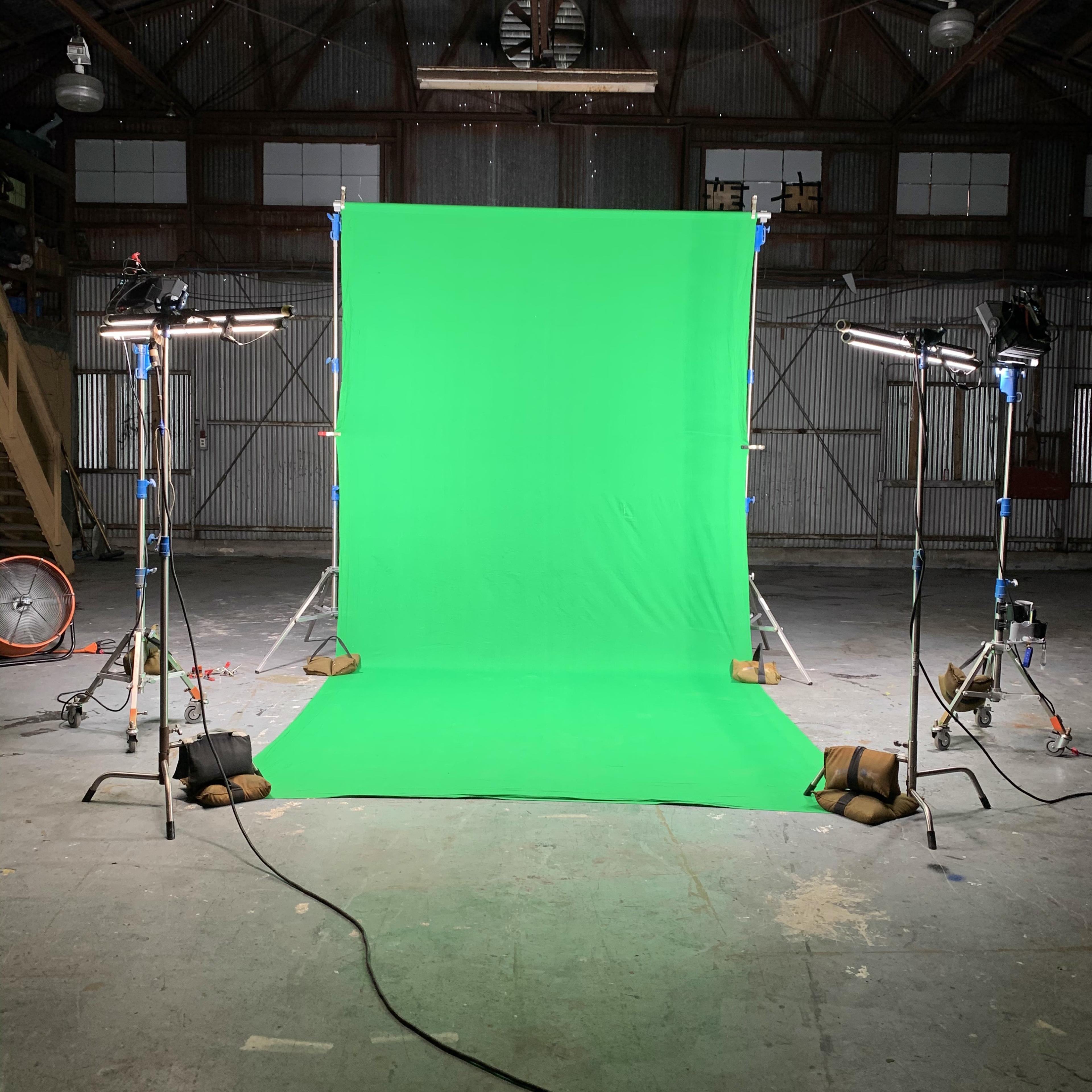 A green backdrop set up in an industrial space, illuminated by two lights on tripods.
