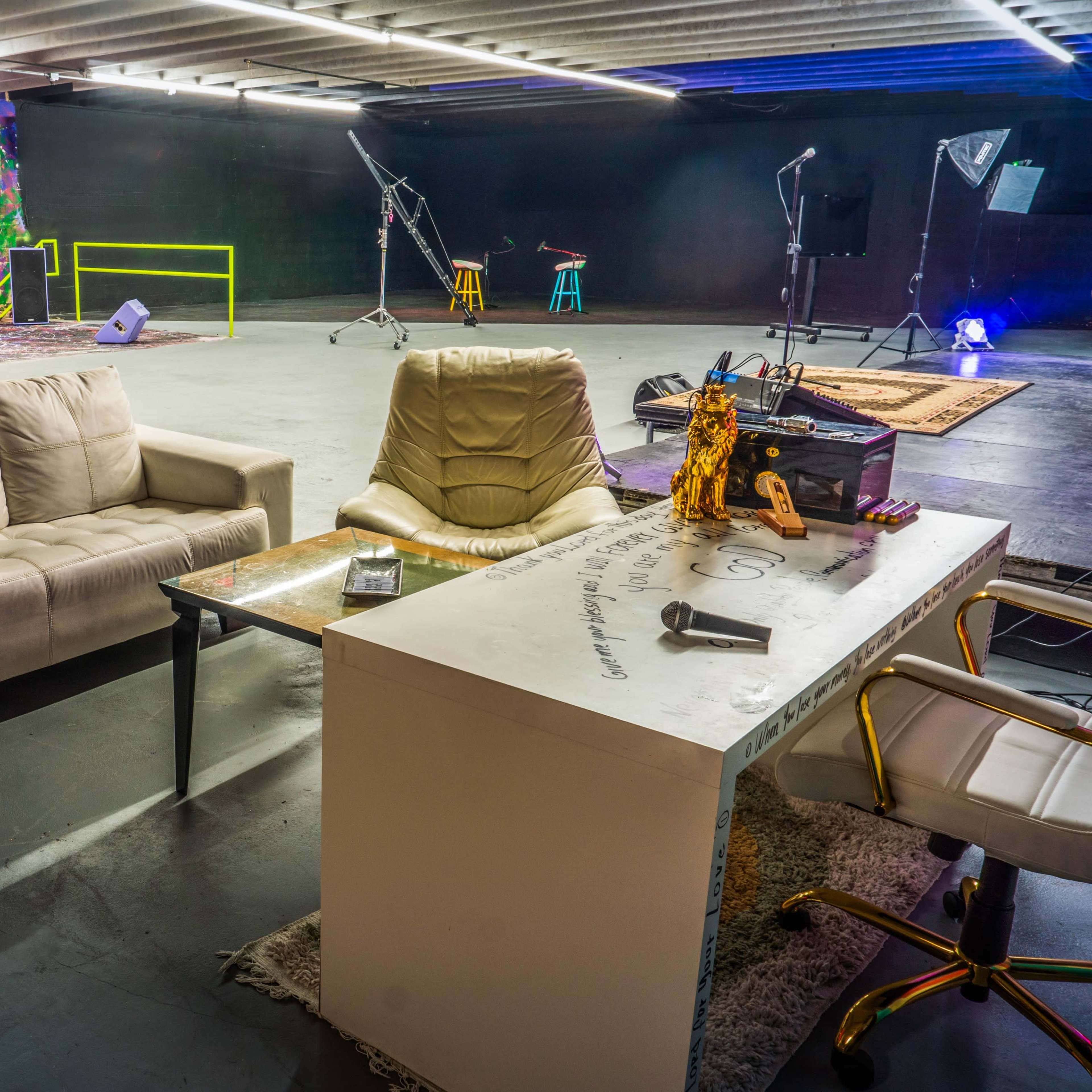 A spacious studio with two sofas, a desk with chairs, and colorful lighting in the background.