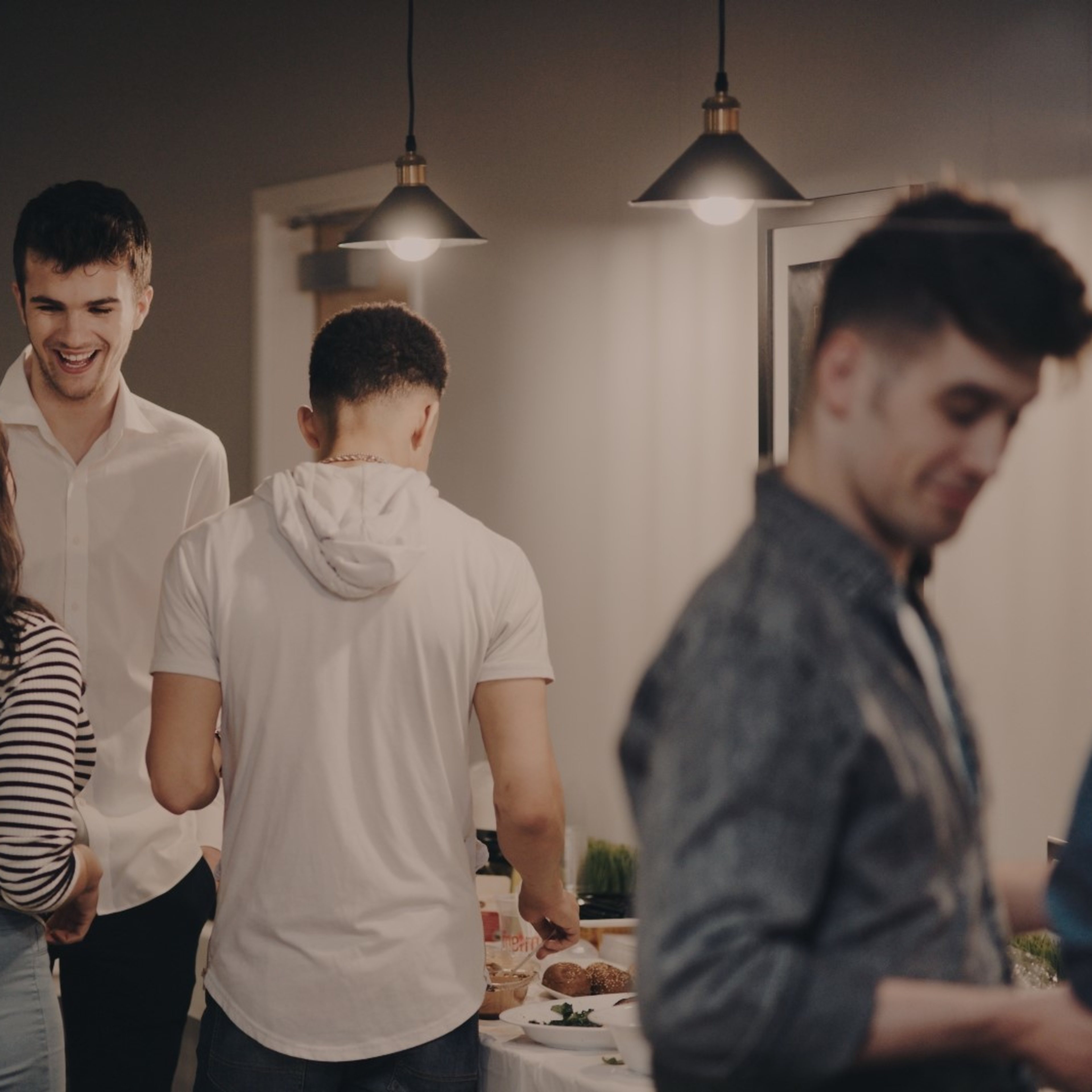 A group of four people engages in conversation and prepares food at a social gathering in a well-lit room.