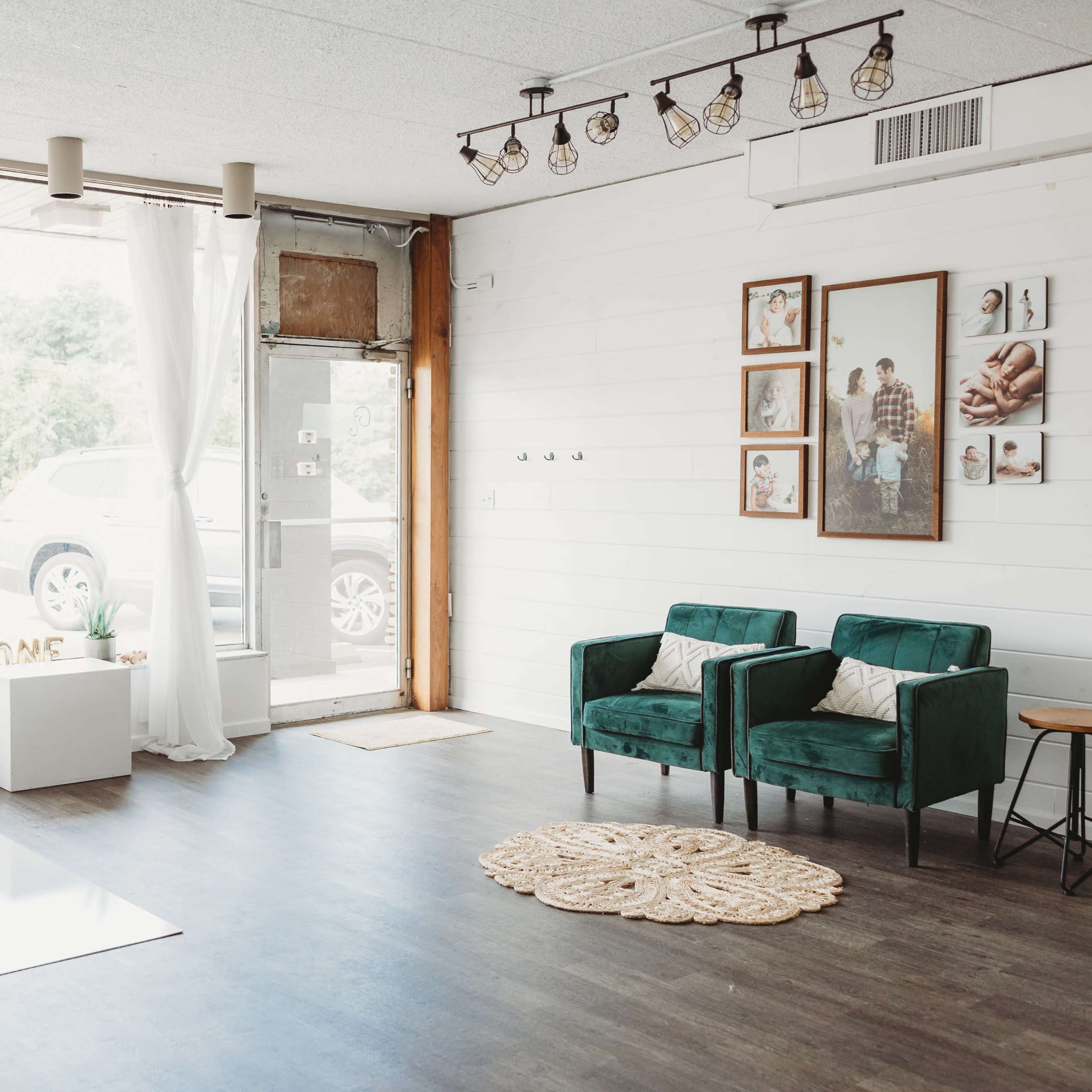 A bright, minimalist interior space with two green armchairs, a white backdrop, and large windows allowing natural light to enter.