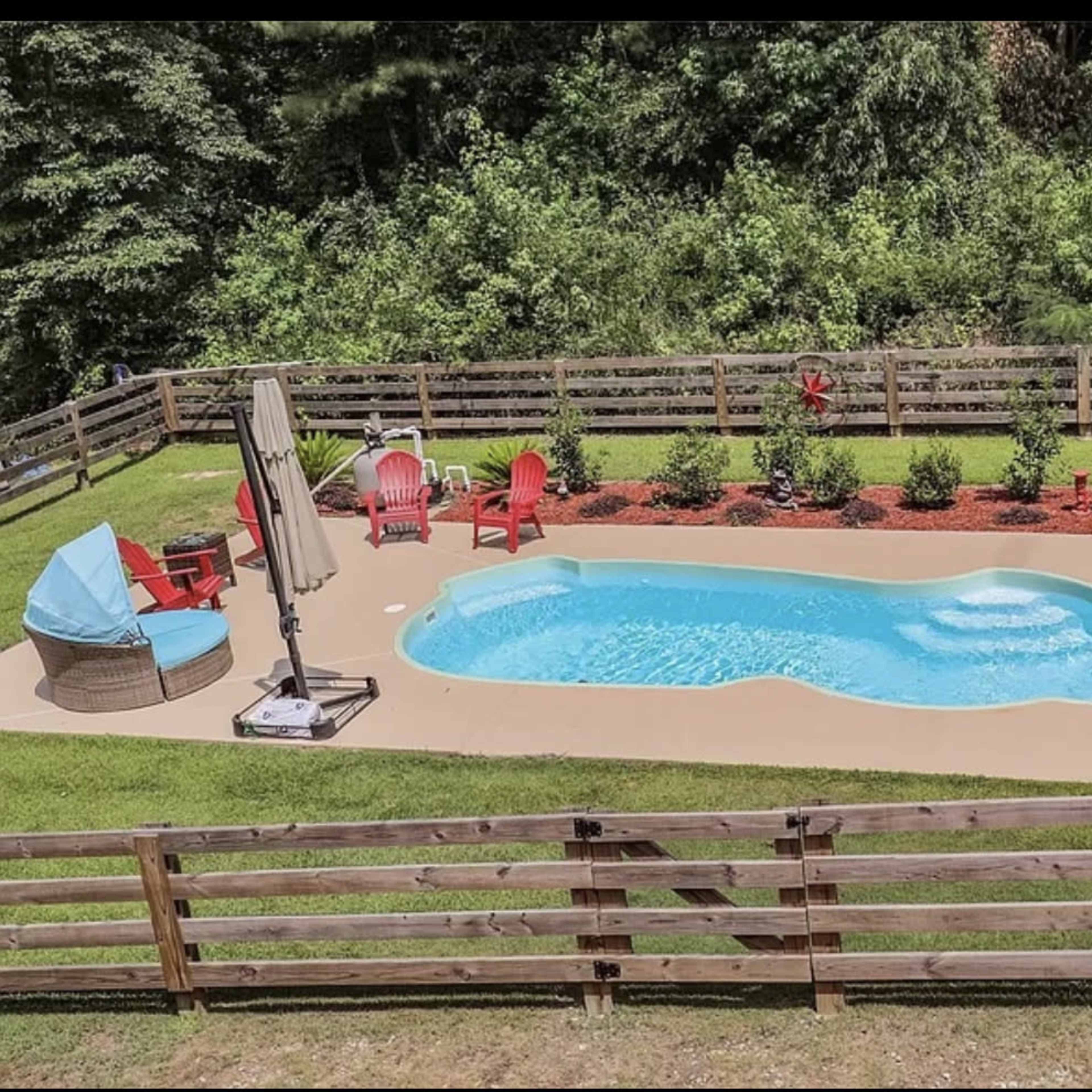 A backyard with a pool surrounded by landscaped grass, lounge chairs, and decorative plants.