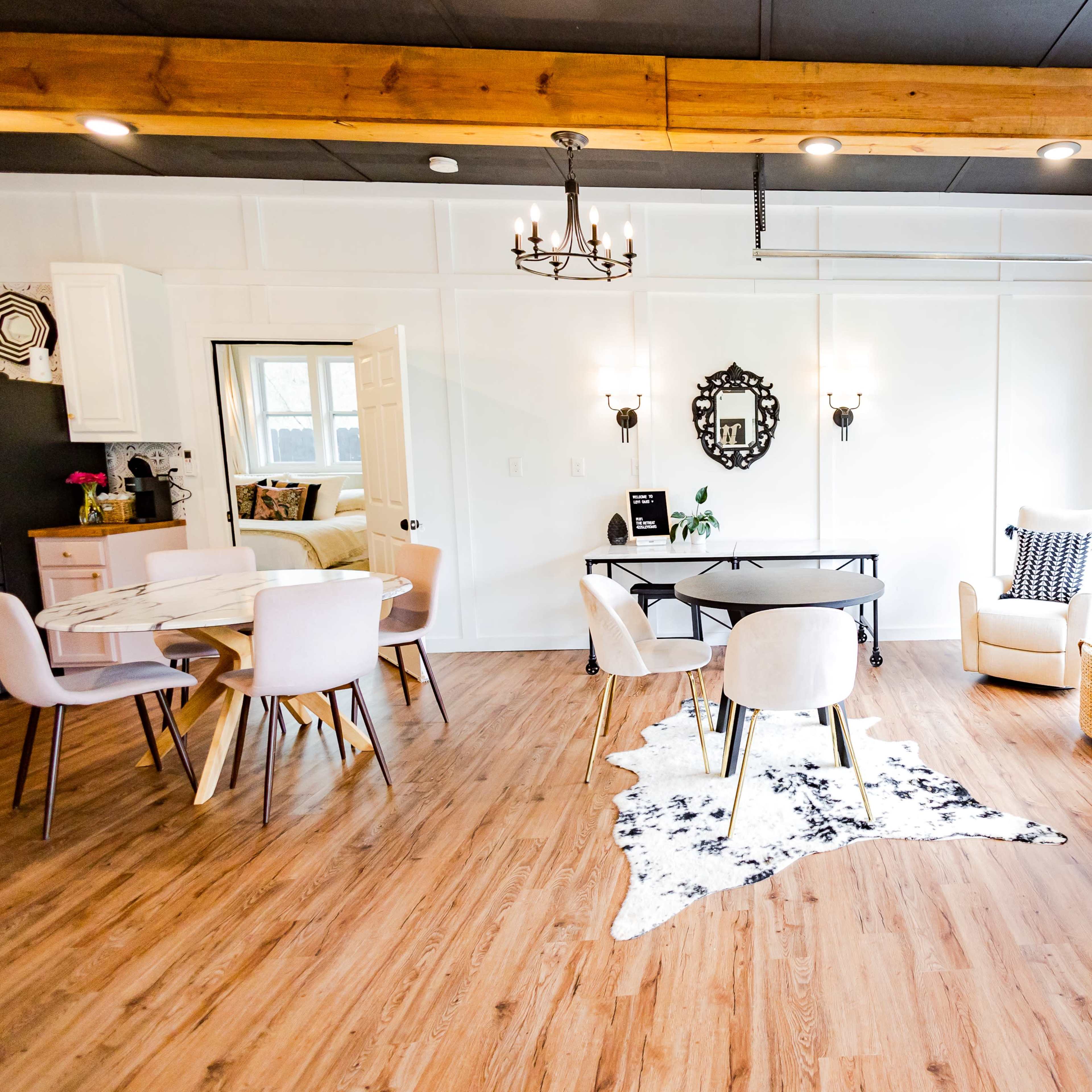A modern interior design of a dining and living area featuring a table with chairs, a cozy seating arrangement, and large windows allowing natural light.