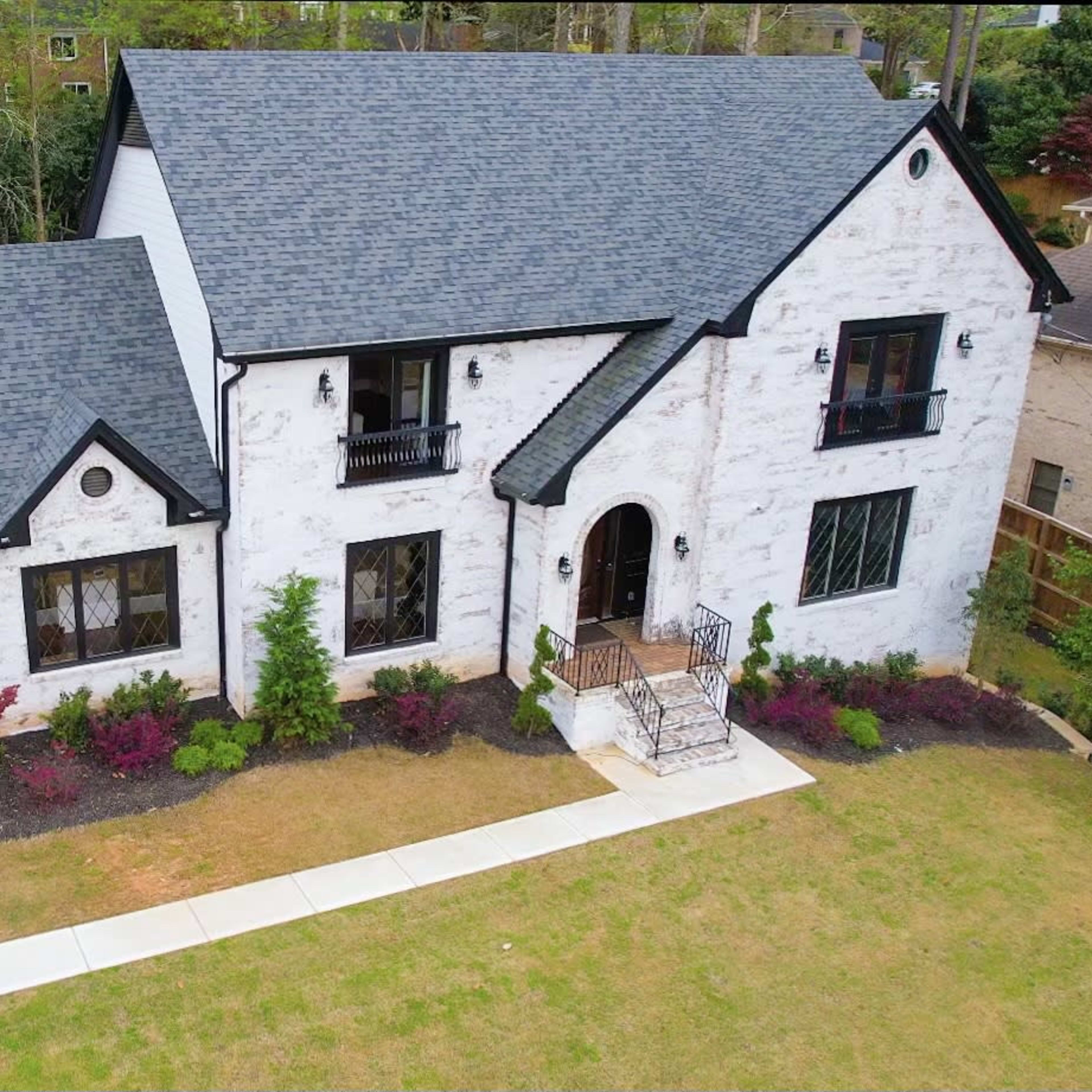 A large, two-story white house with a dark roof and landscaped garden is pictured from above.