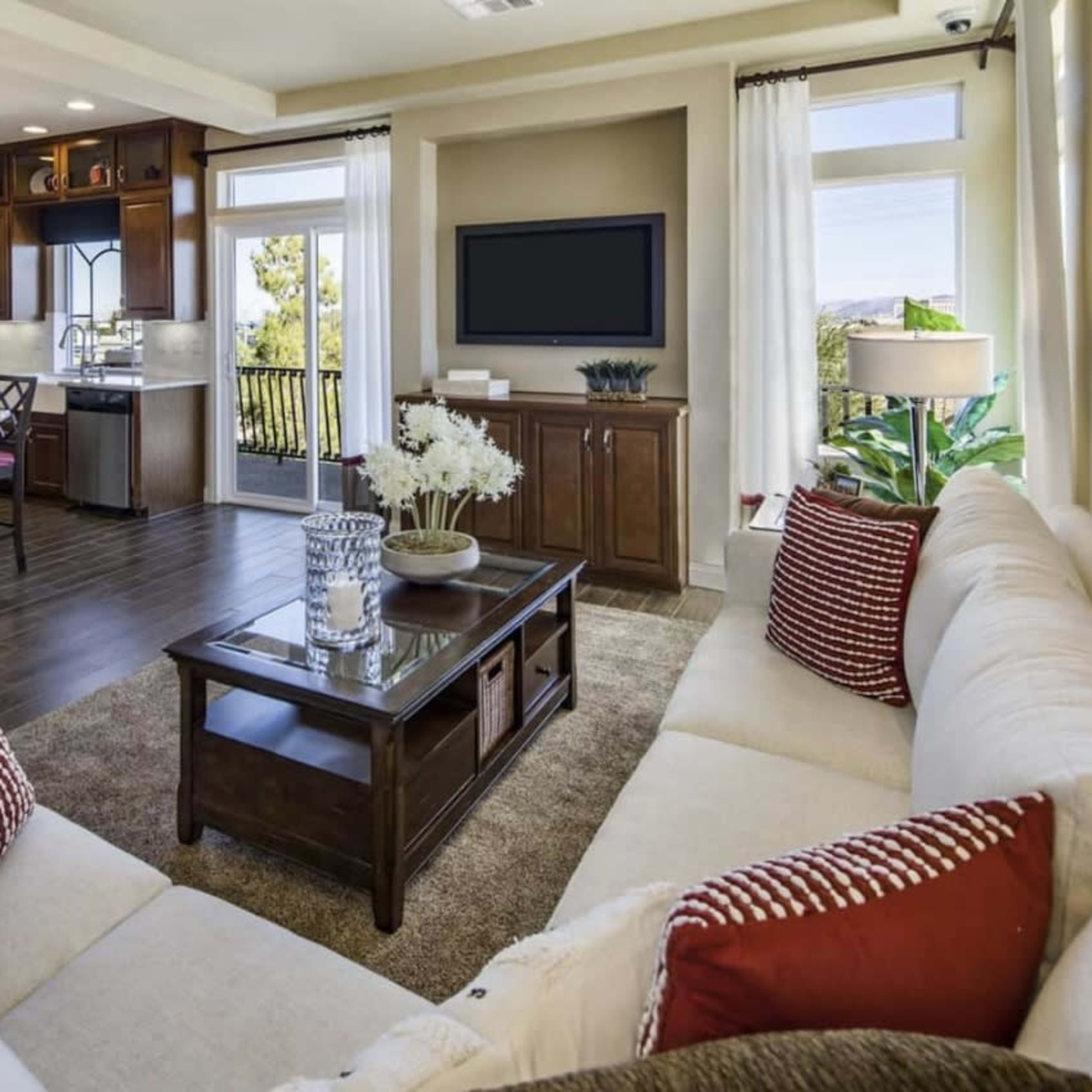 A modern living room with a cream-colored sofa, a wooden coffee table, and an open kitchen in the background, featuring dark cabinetry and a dining area.