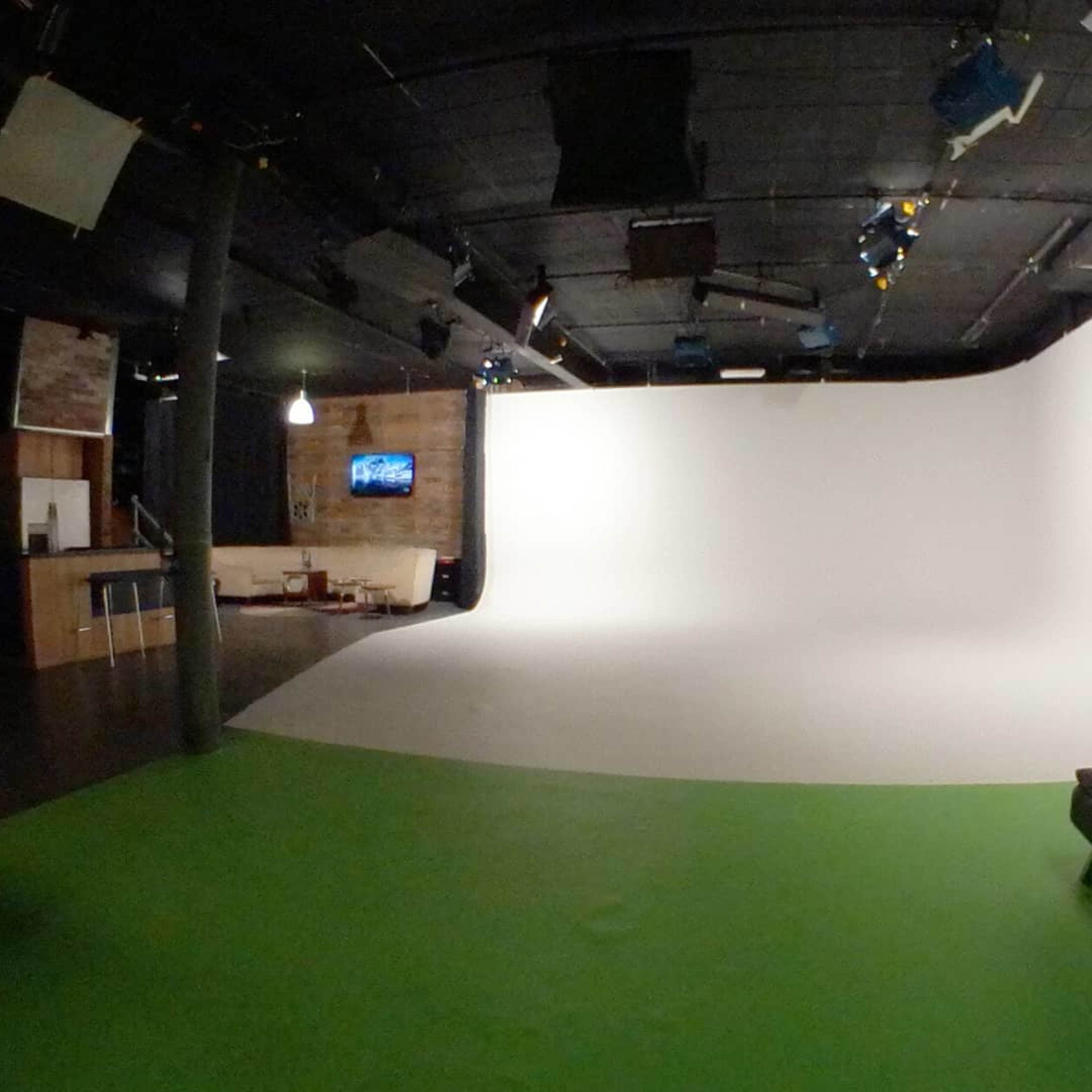 A studio space featuring a green floor, a white backdrop, and a black couch in the foreground.