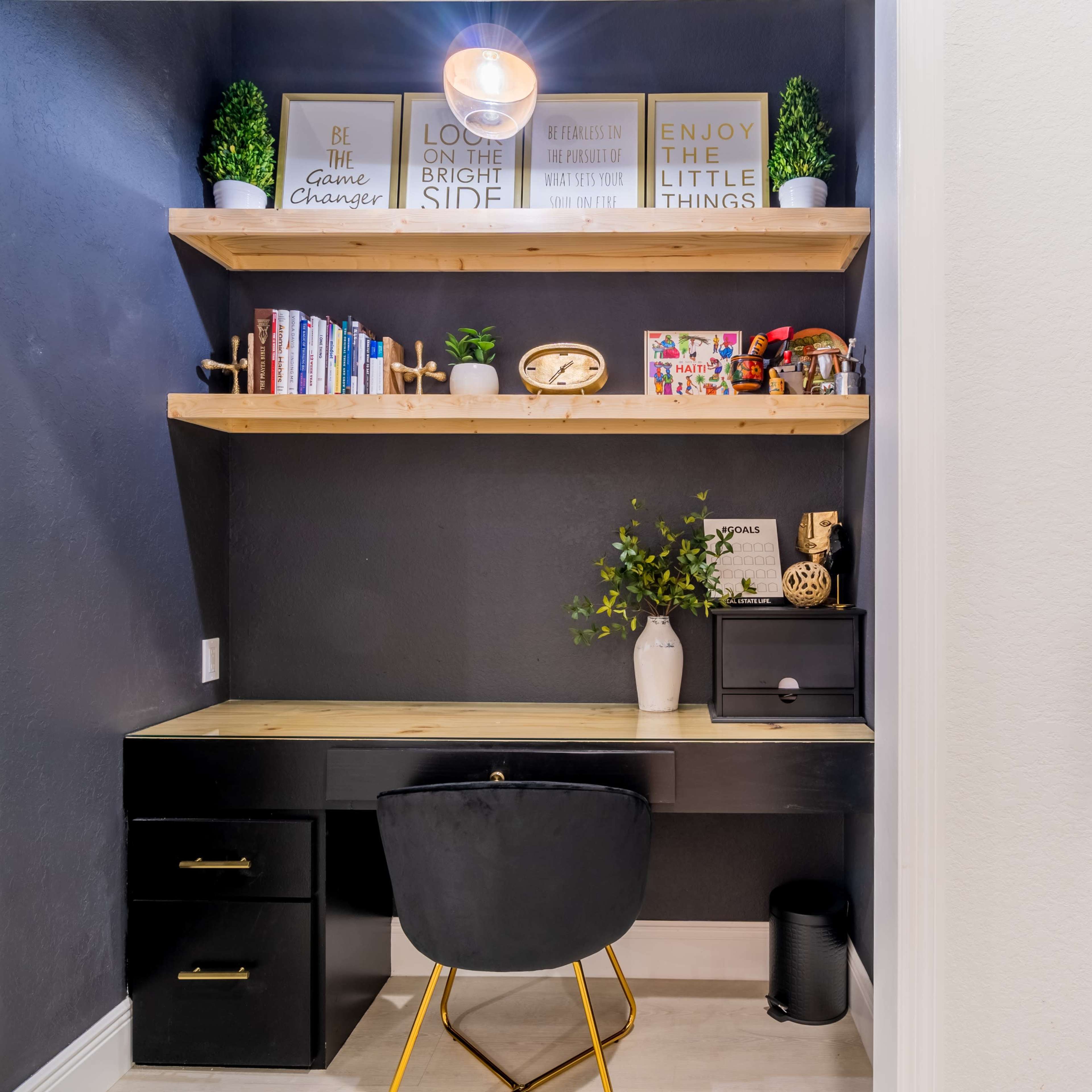A modern home office setup with a wooden desk, shelves filled with books and decorative items, and a stylish chair beside a hallway featuring a sideboard and wall art.