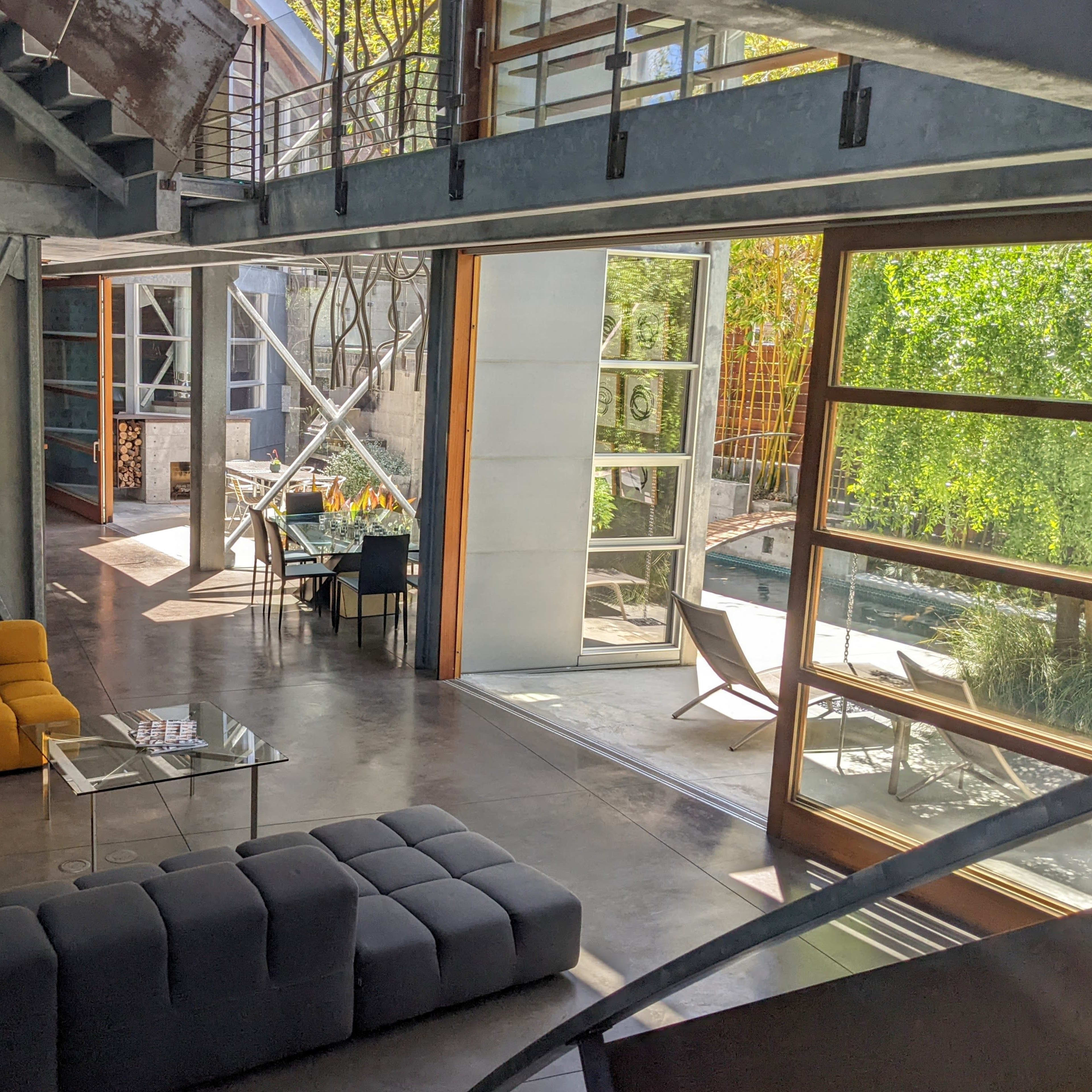 A modern living area with a gray and yellow sectional sofa, large glass walls, and a view of an outdoor space featuring a pool and seating.