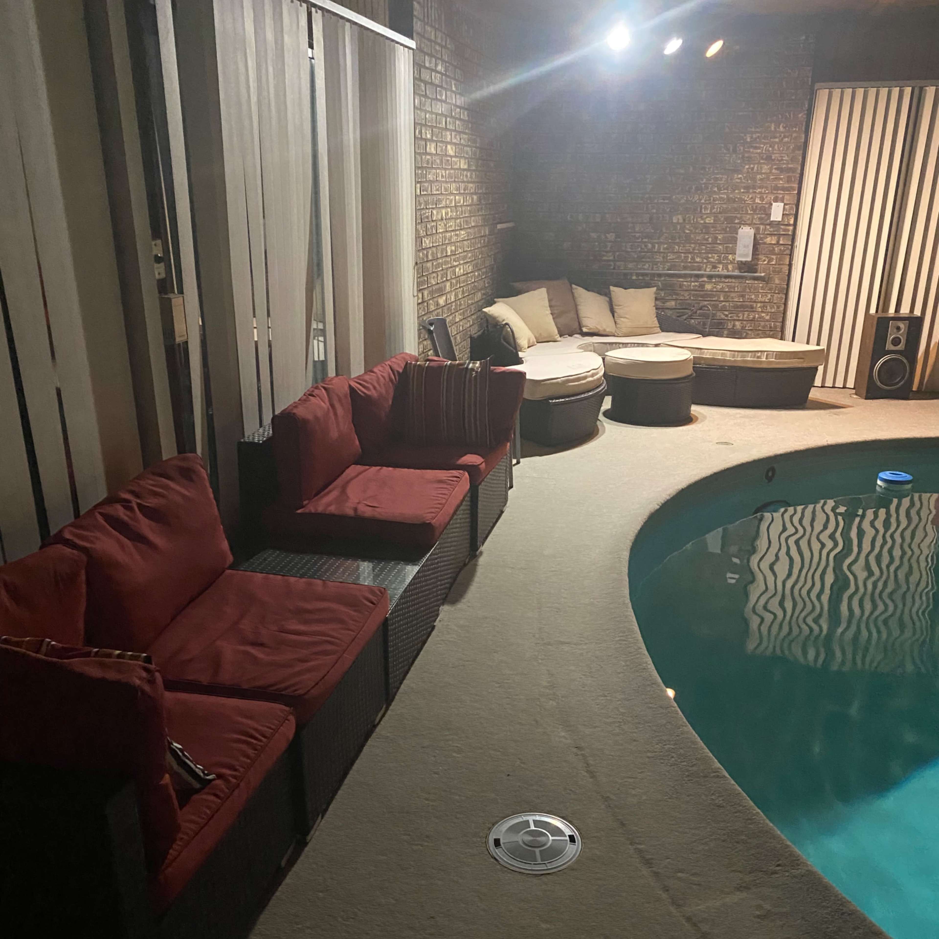 A lounge area featuring red cushioned seating and a circular pool is enclosed by glass sliding doors and light-colored walls.