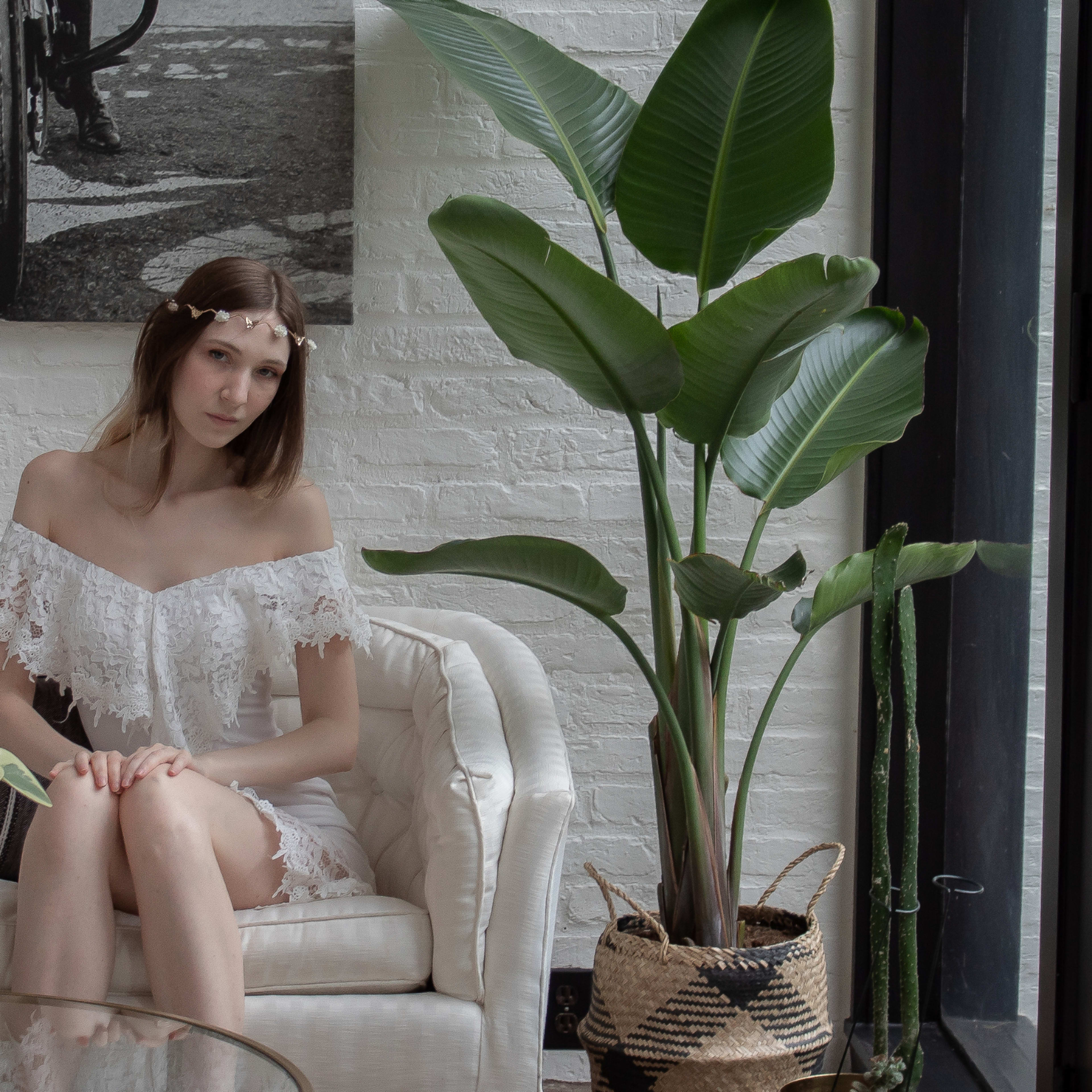A woman sits on a white chair next to a large leafy plant in a bright, modern interior space.