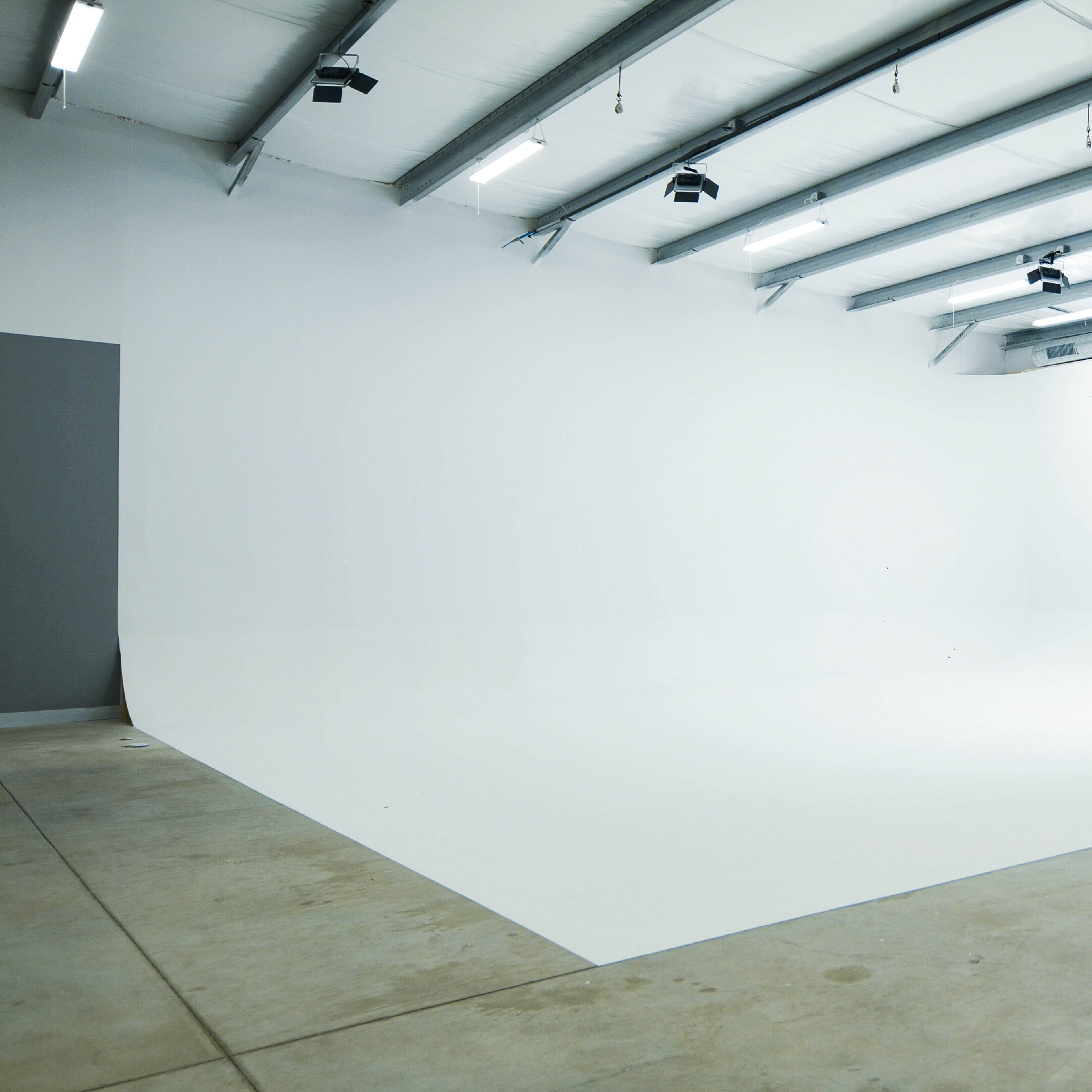 An empty photo studio with a seamless white backdrop and overhead lighting fixtures.