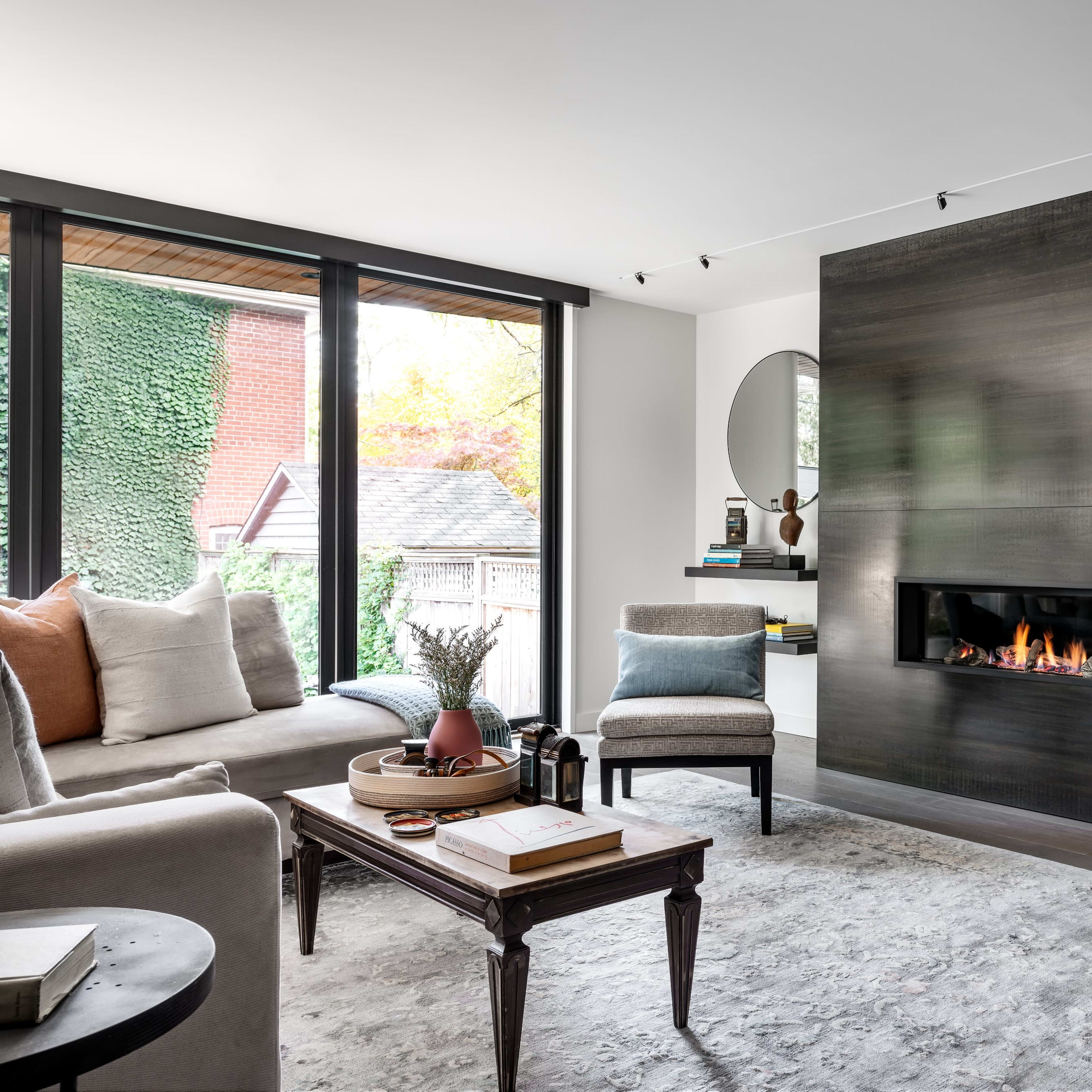 A modern living room features a sleek fireplace on a dark wall, flanked by mirrors, with a cozy seating arrangement and decorative shelves.