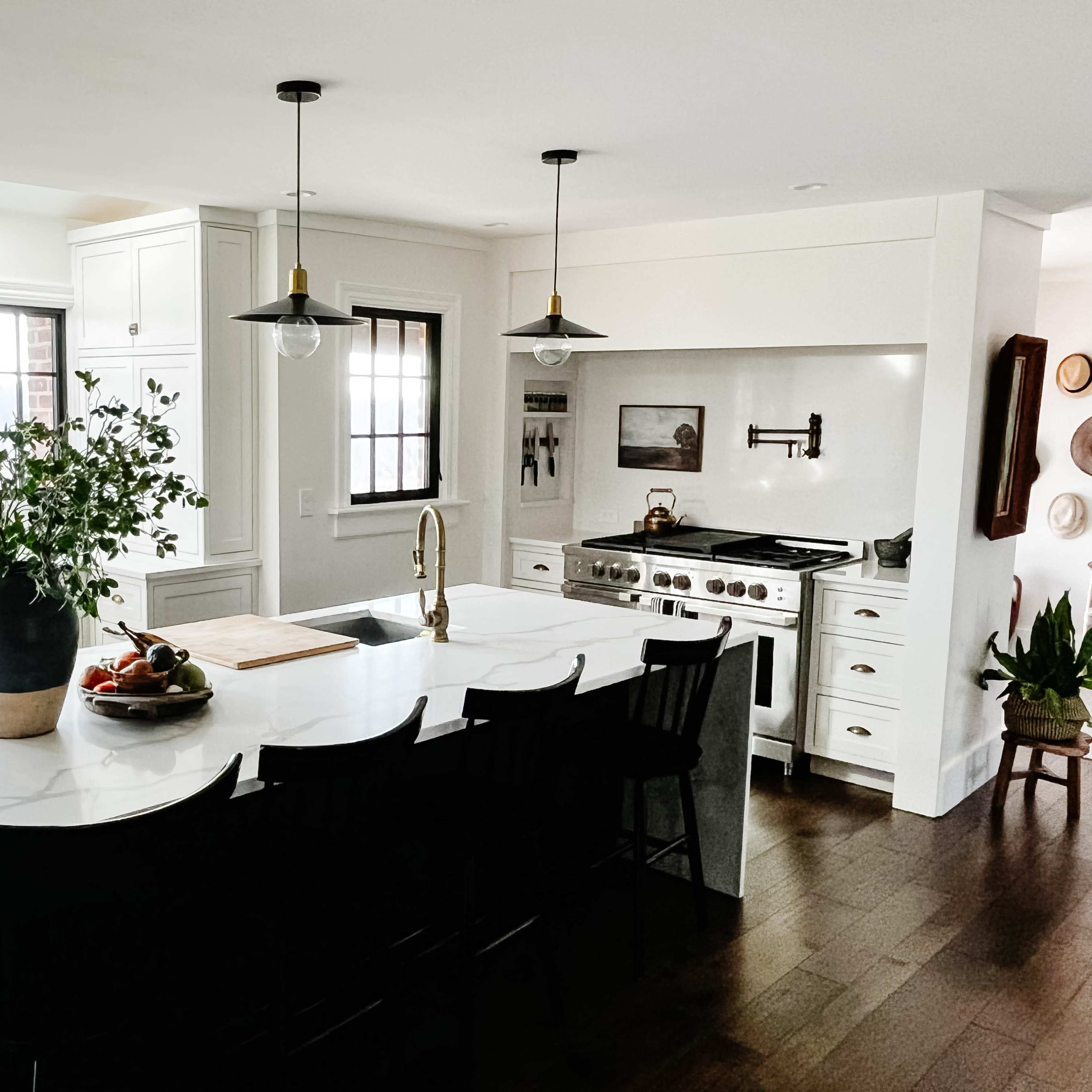 A modern kitchen features a white marble island with a black seating area, a large stove, and natural light from a window.