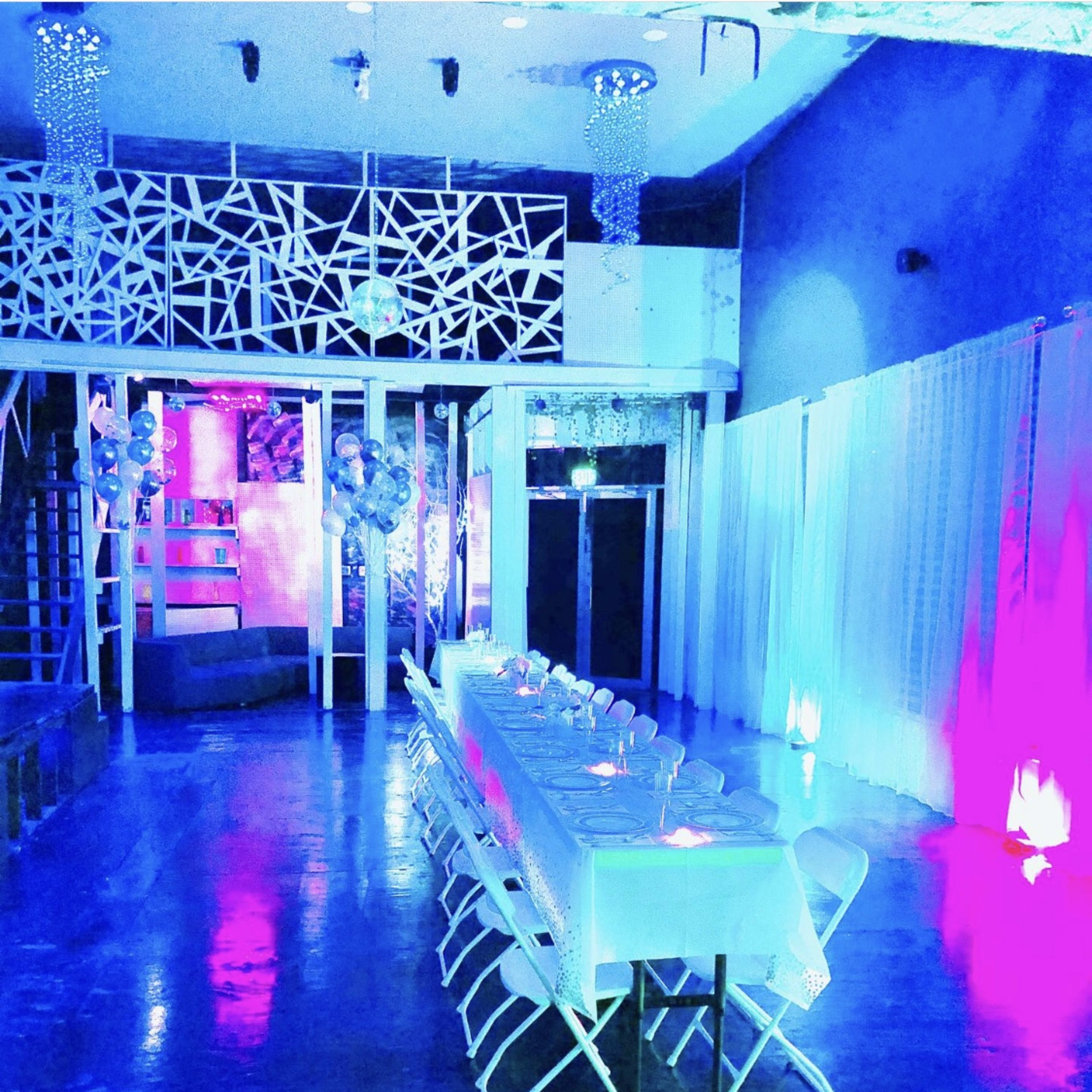 A long, elegantly set table is arranged in a brightly lit event space with colorful lighting and decorative elements.