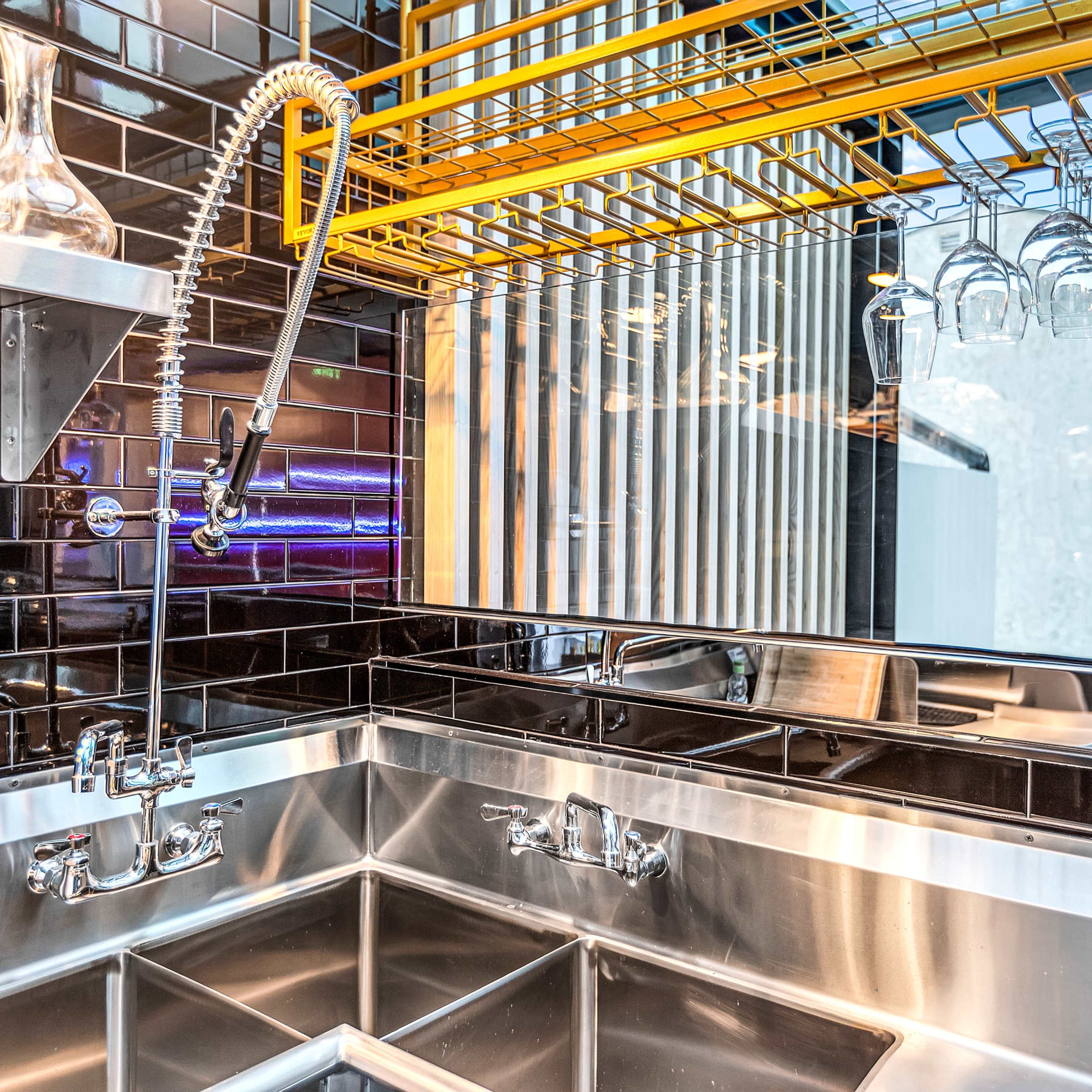 A modern kitchen sink area with stainless steel fixtures, a wall-mounted spray faucet, and a rack for hanging glassware.