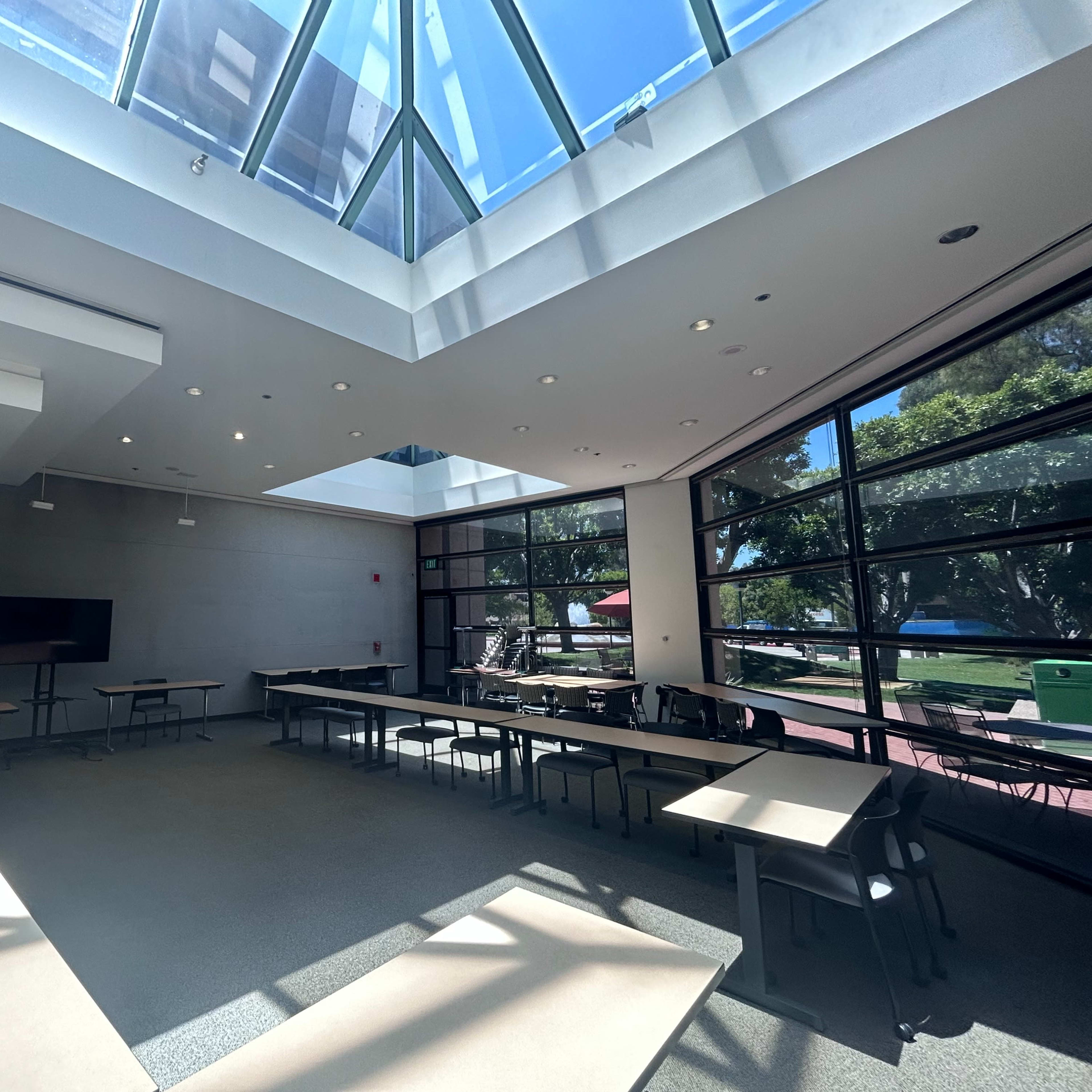 A spacious conference room with large windows, a skylight, and several tables arranged for meetings.