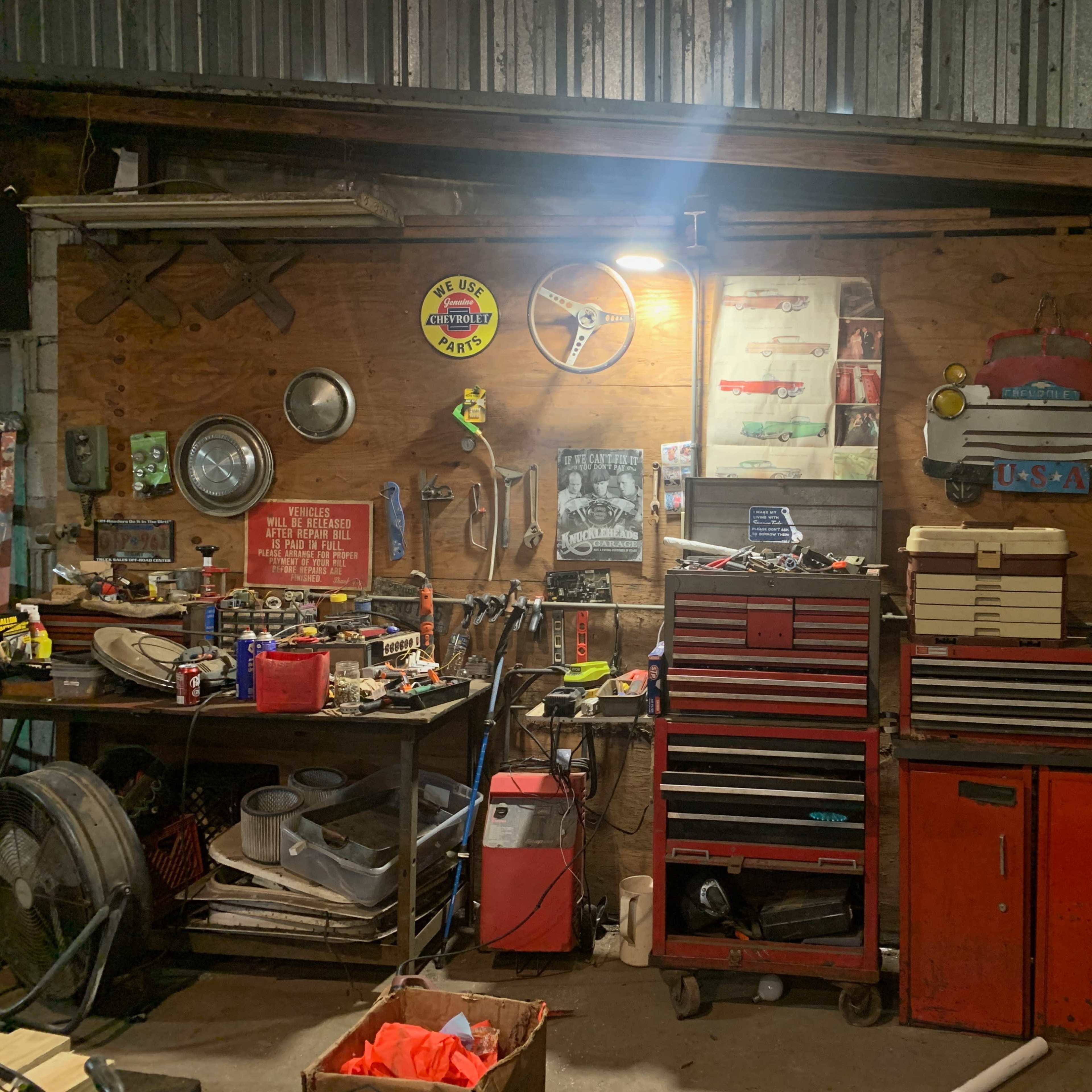 A cluttered workshop with various tools, boxes, and automotive memorabilia displayed on a wooden wall.