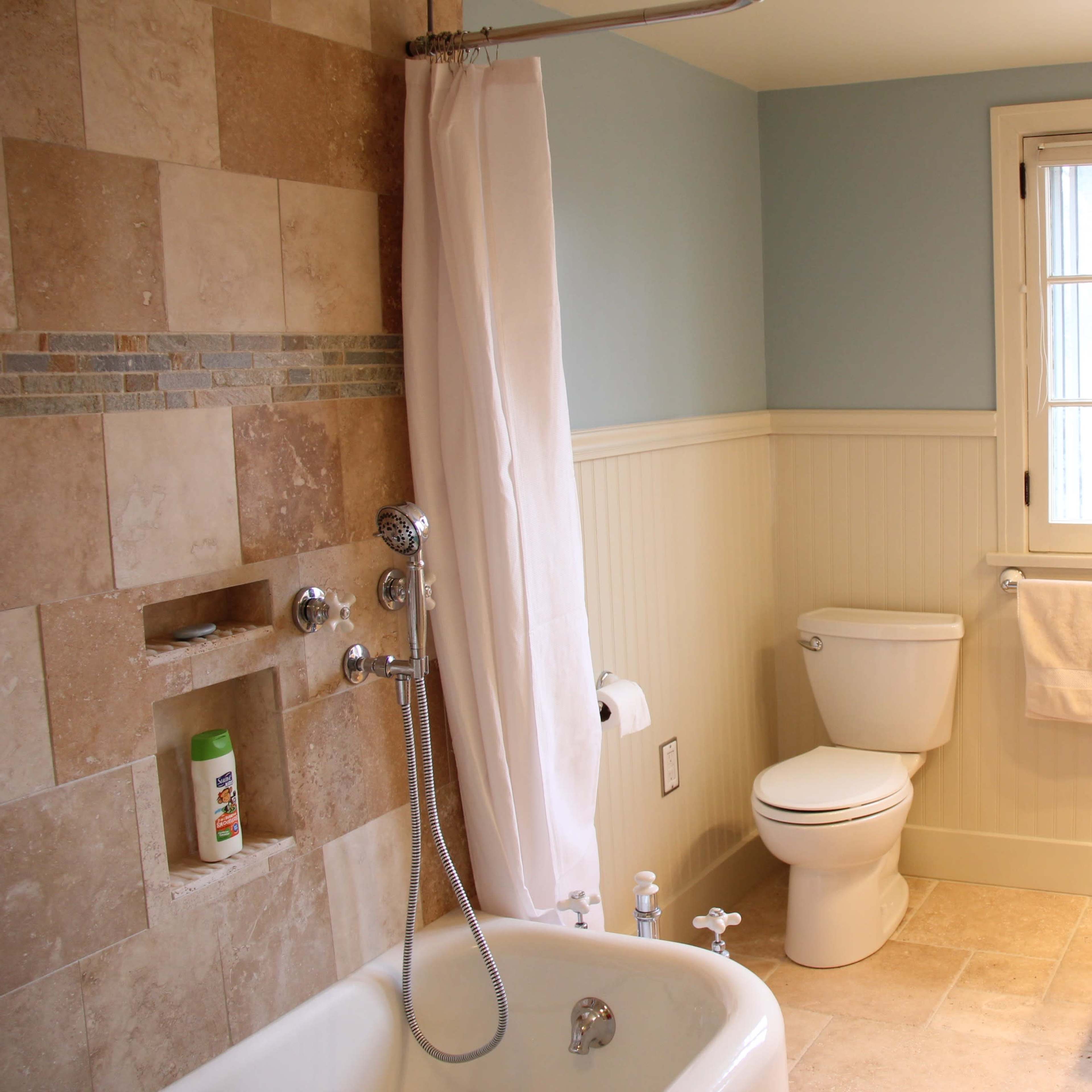 A bathroom featuring a bathtub with a shower, a toilet, and a sink, all surrounded by light-colored tile and blue-painted walls.