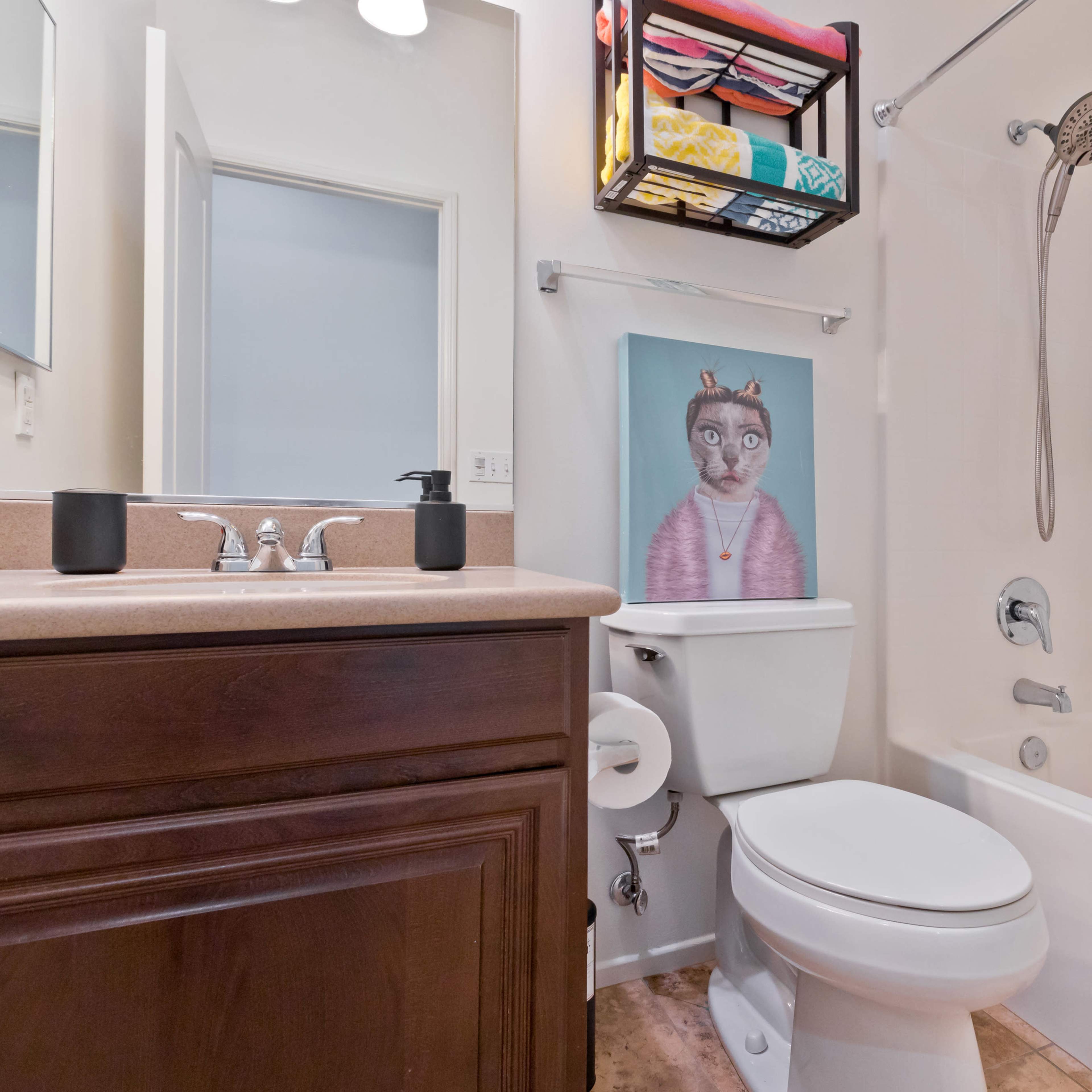 A bathroom featuring a bathtub, a toilet, a sink with a mirror above, and a colorful shelf holding various items.