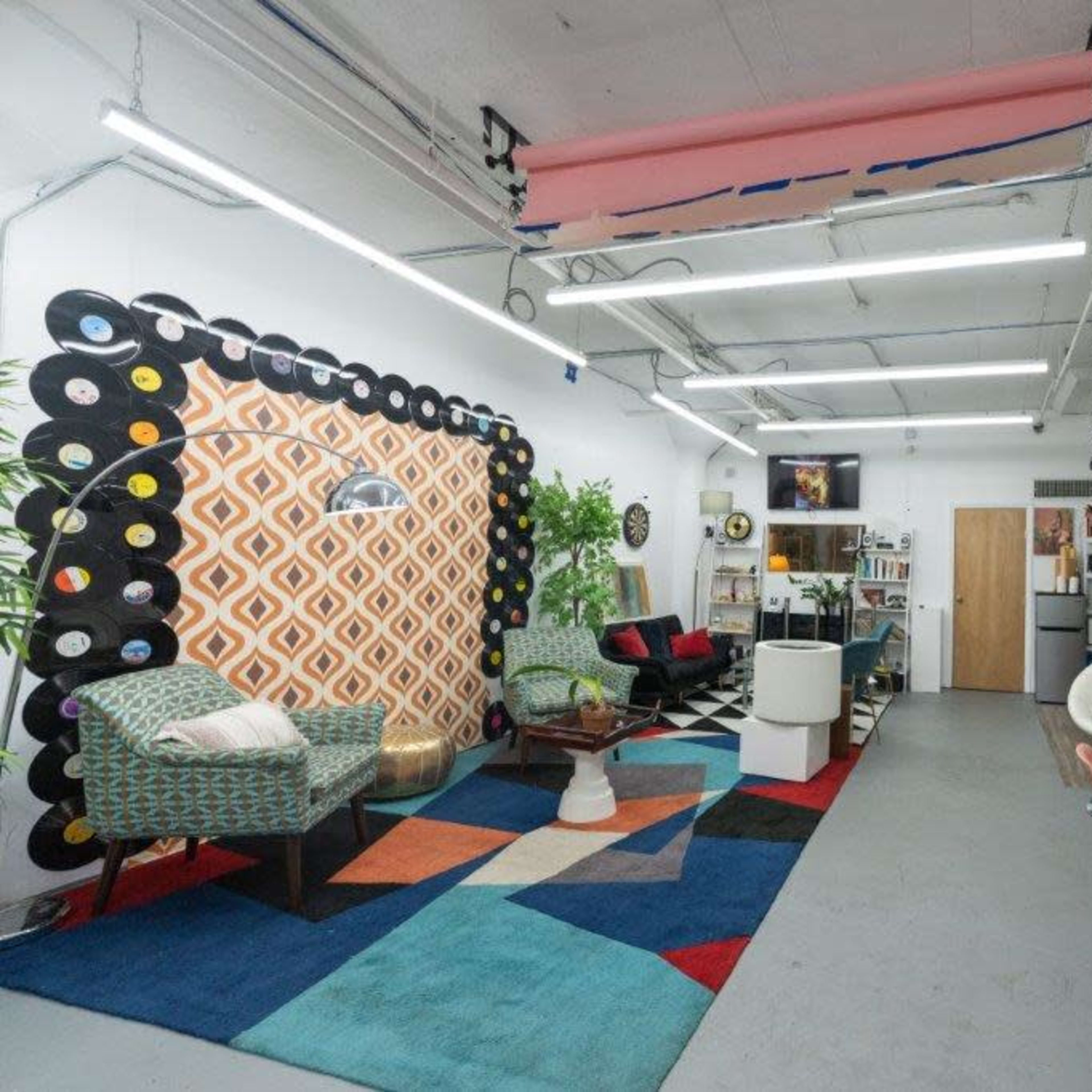 A spacious, modern room with colorful furniture, a patterned rug, and decorative wall accents featuring vinyl records and flowers.