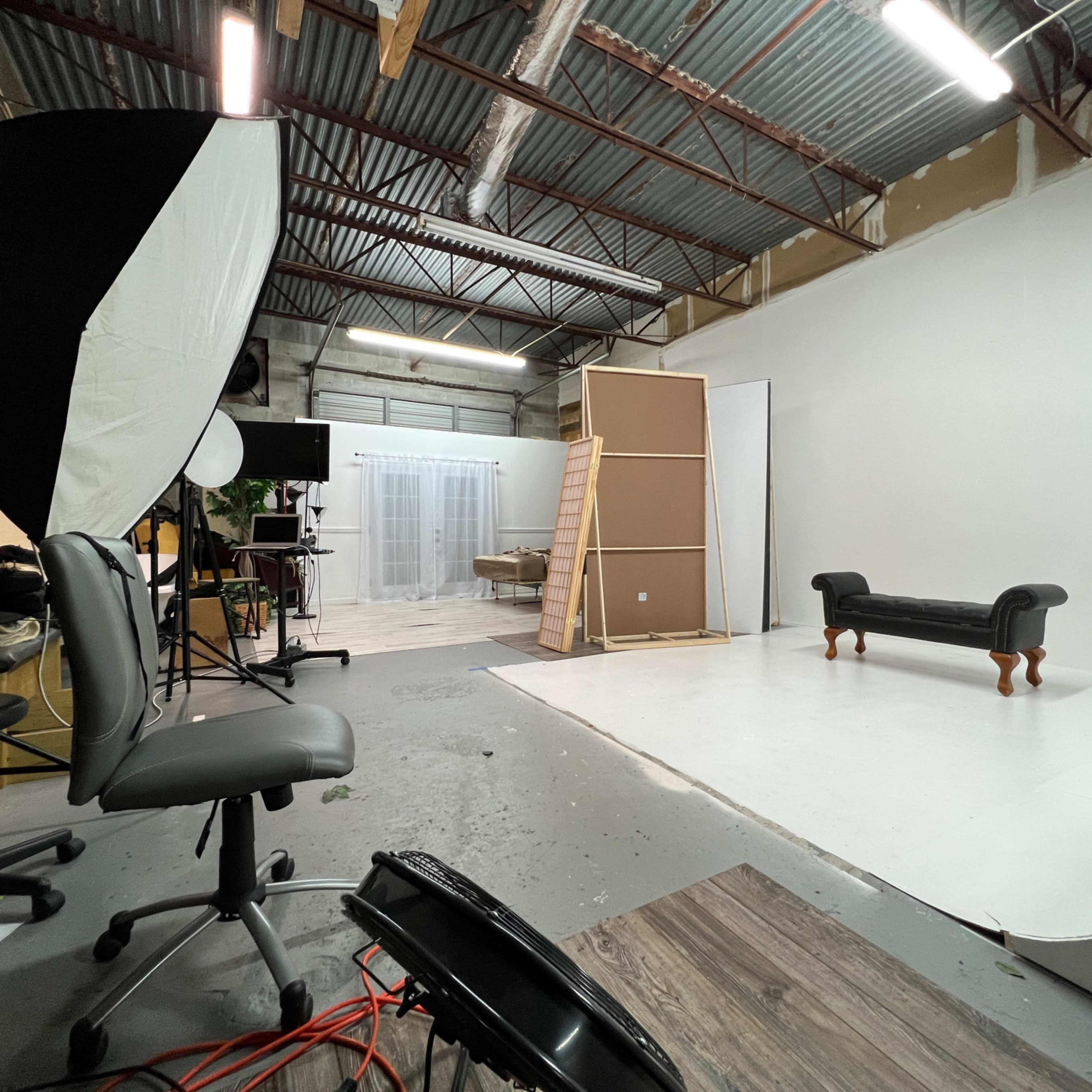 A photography studio with a white backdrop, a black couch, and various equipment arranged around the space.